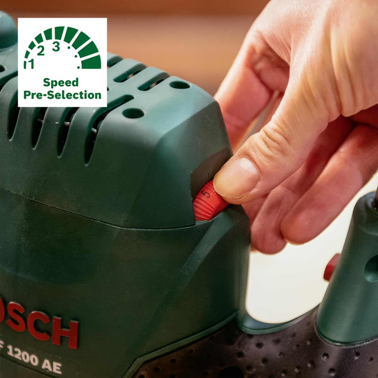 Hand verstellt das rote Geschwindigkeitswahlrad einer grünen Bosch-Fräse mit eingeblendetem Tachometer-Symbol.