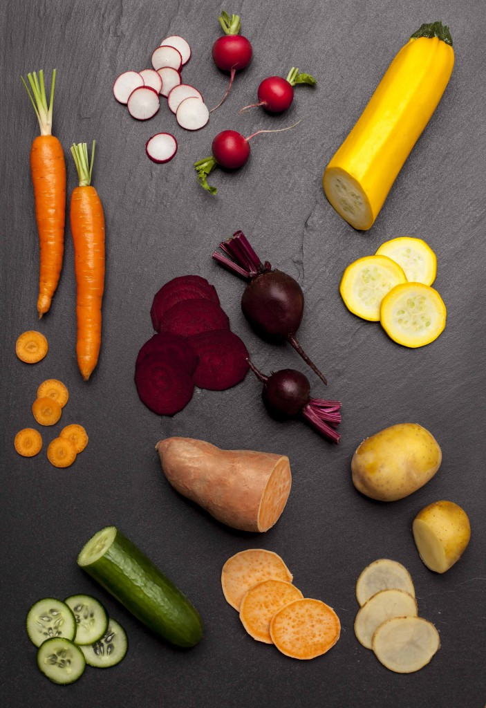 Verschiedenes frisches Gemüse wie Möhren, Radieschen, Rote Bete und Kartoffeln auf dunklem Schiefer.