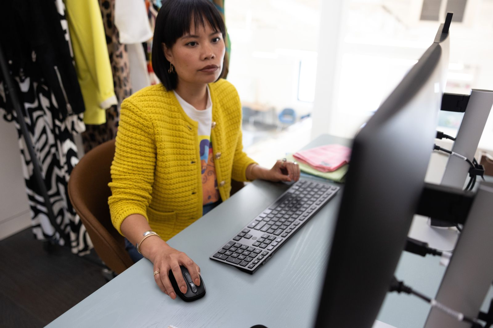 Eine Frau in gelber Jacke sitzt an einem Schreibtisch und arbeitet am Computer in einem Büro.