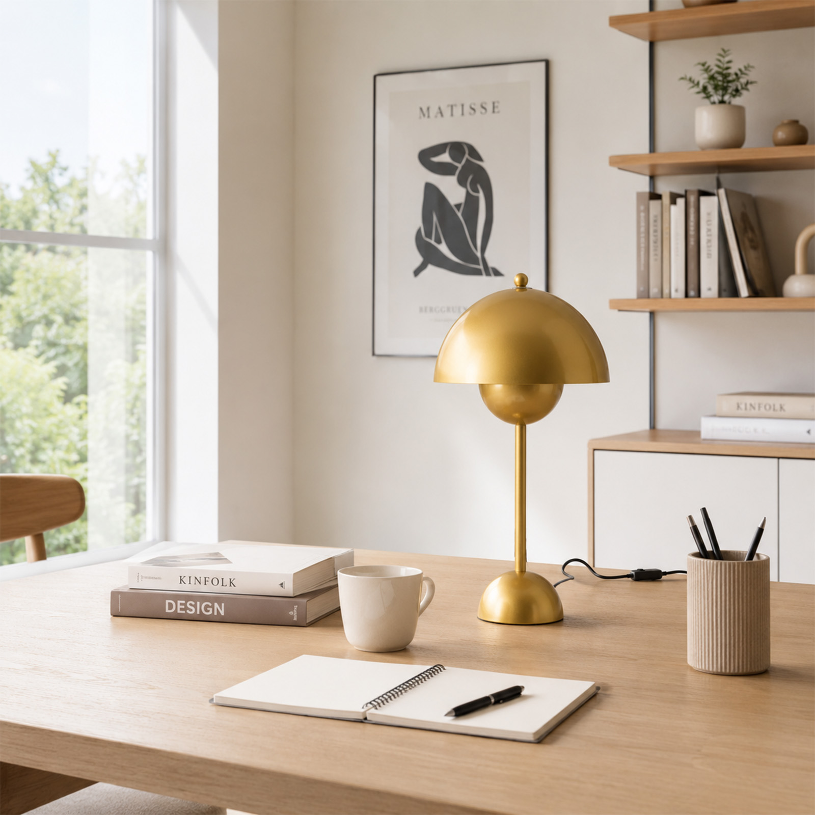 Un escritorio de madera con lámpara dorada, libros, taza de café y cuaderno en una habitación luminosa.