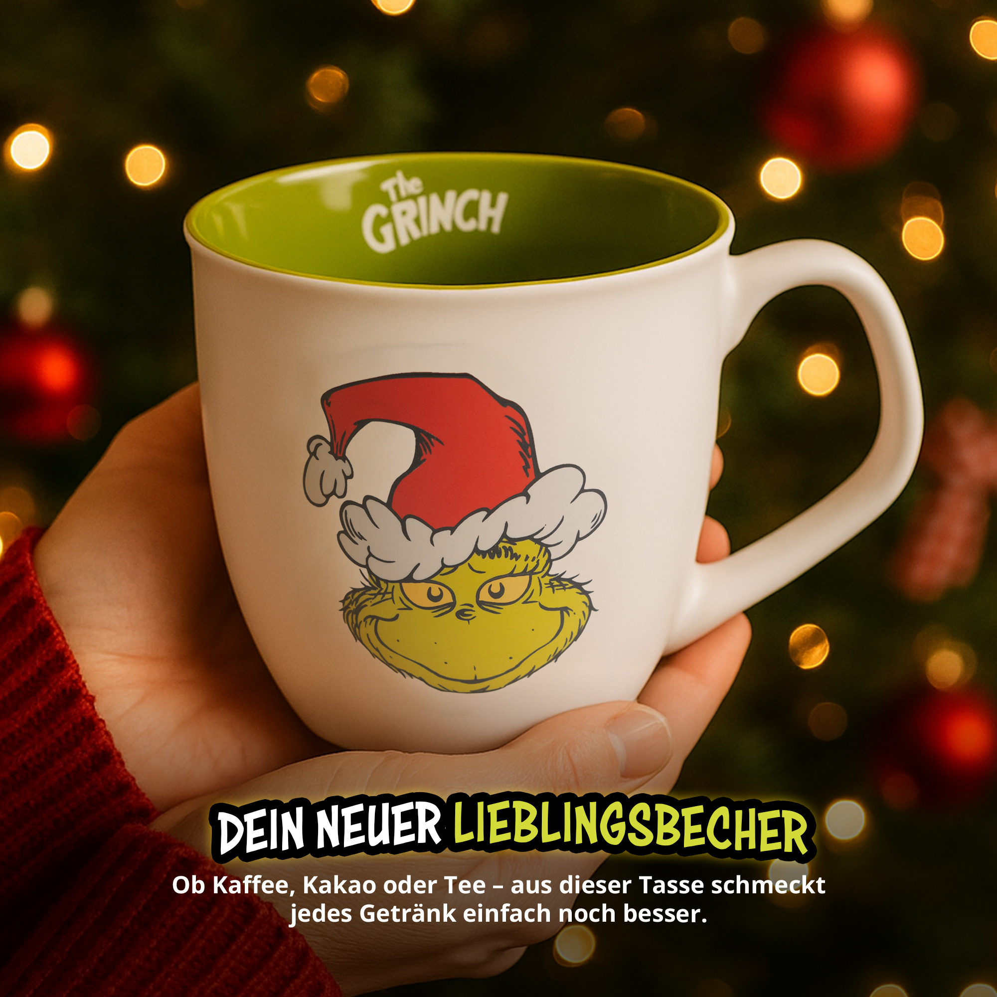 Hände halten weiße Grinch-Tasse mit roter Weihnachtsmütze vor Weihnachtsbaum.