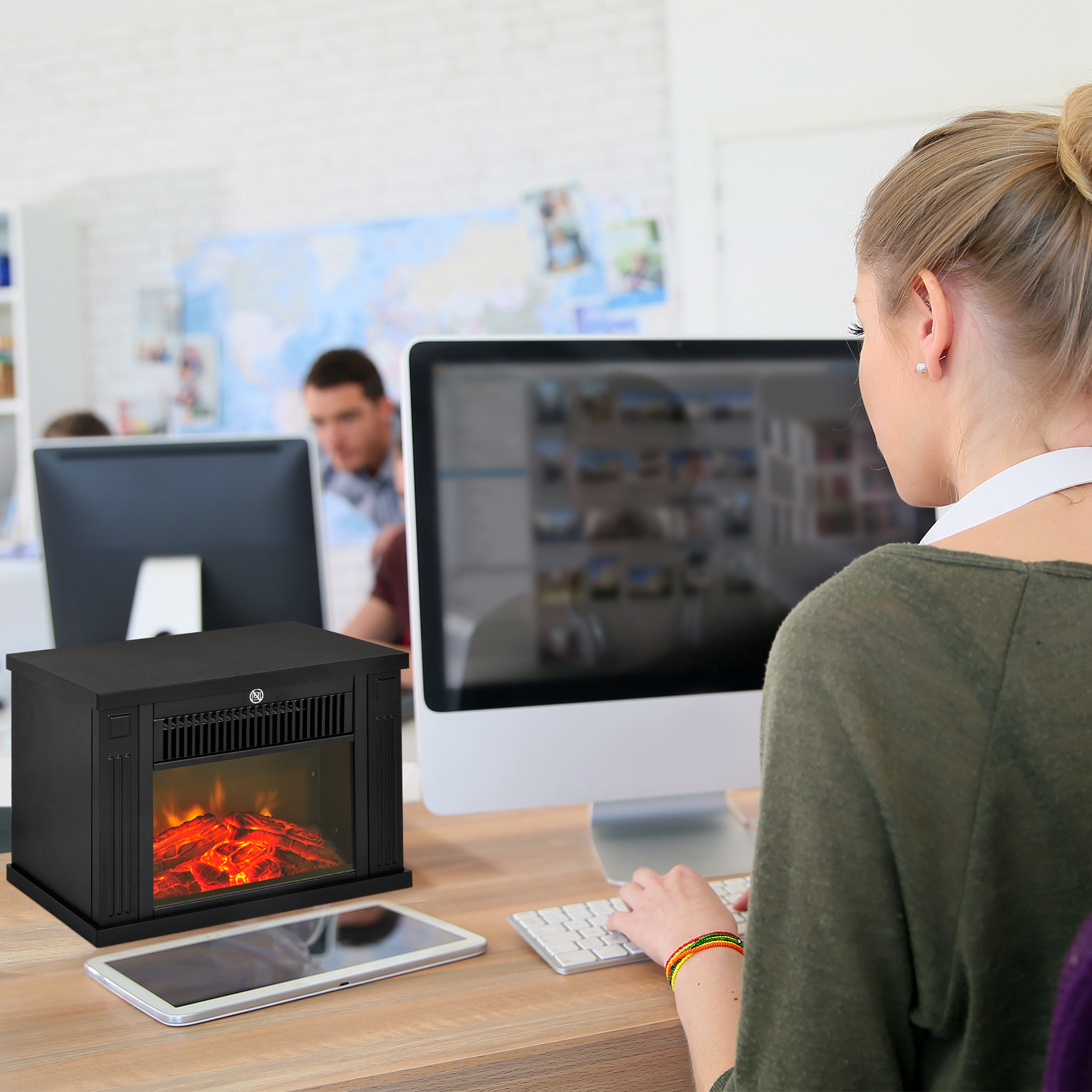 Una mujer trabaja en una computadora en una oficina, junto a ella hay un pequeño calefactor de chimenea negro.