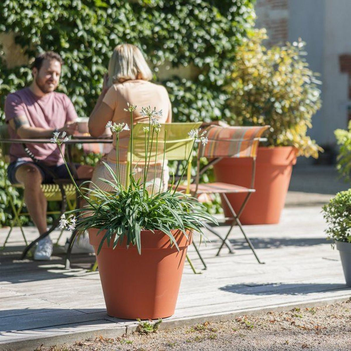 Ein Paar sitzt auf einer Sonnenterrasse mit großen roten Pflanzkübeln.