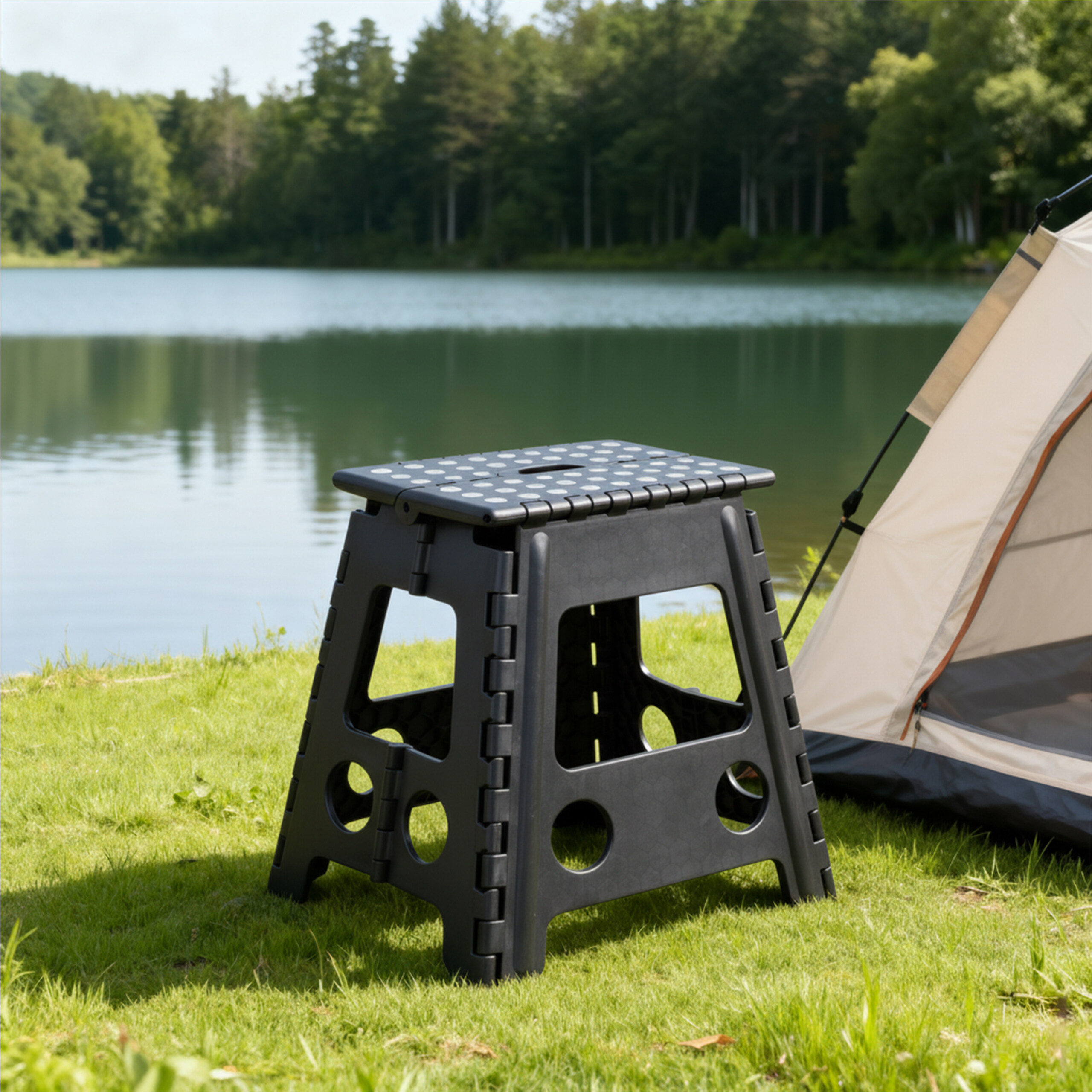 Ein schwarzer Klapphocker steht neben einem Zelt auf einer Wiese am See vor einem Wald.