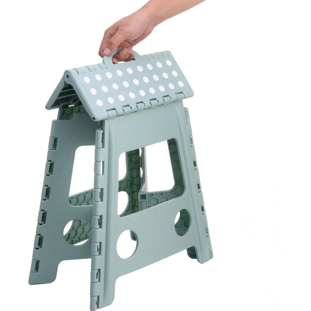 Eine Hand hebt einen zusammenklappbaren, mintgrünen Hocker mit weißen Punkten oben an.
