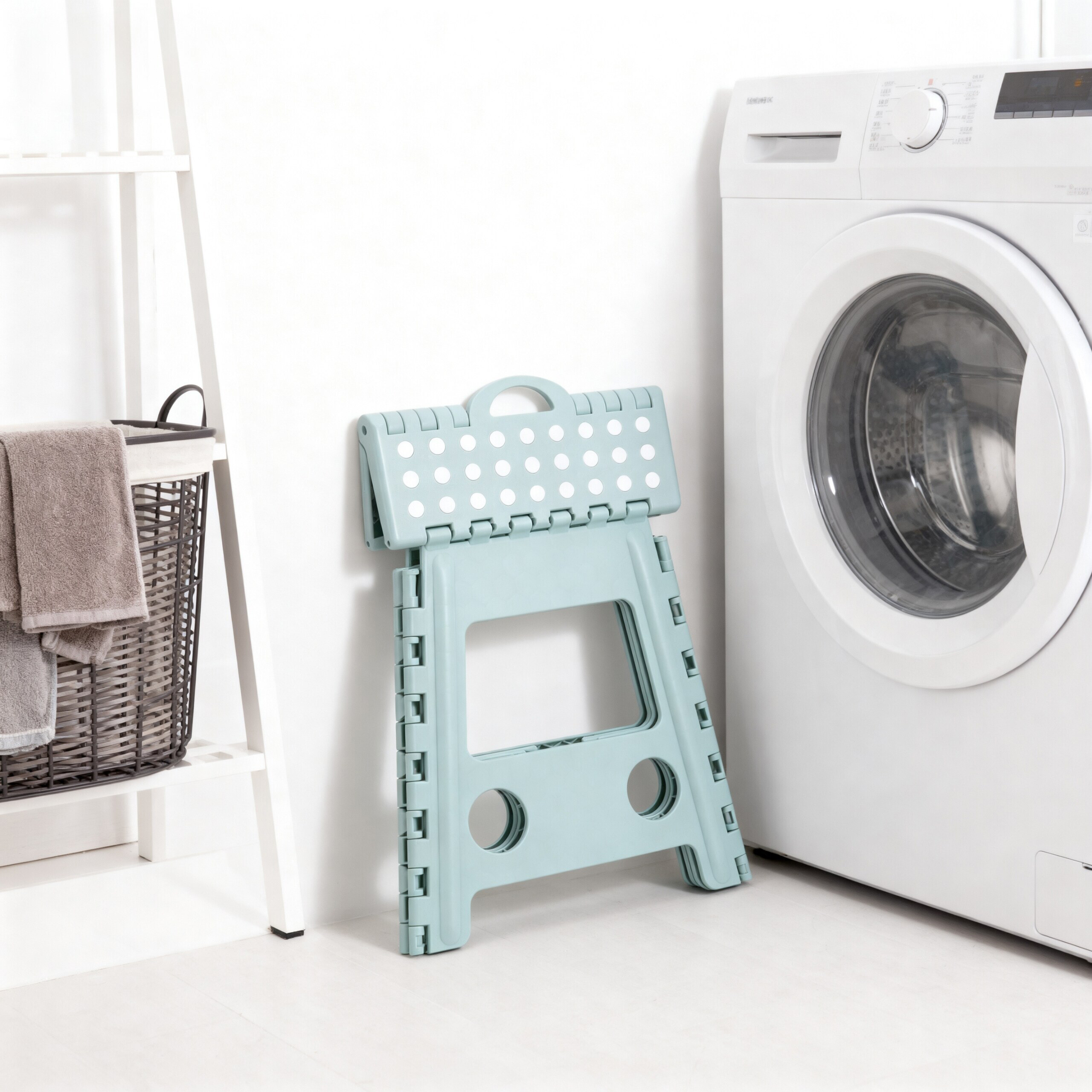 Ein blauer Klapphocker steht in einer hellen Waschküche neben einer Waschmaschine und einem Wäschekorb.