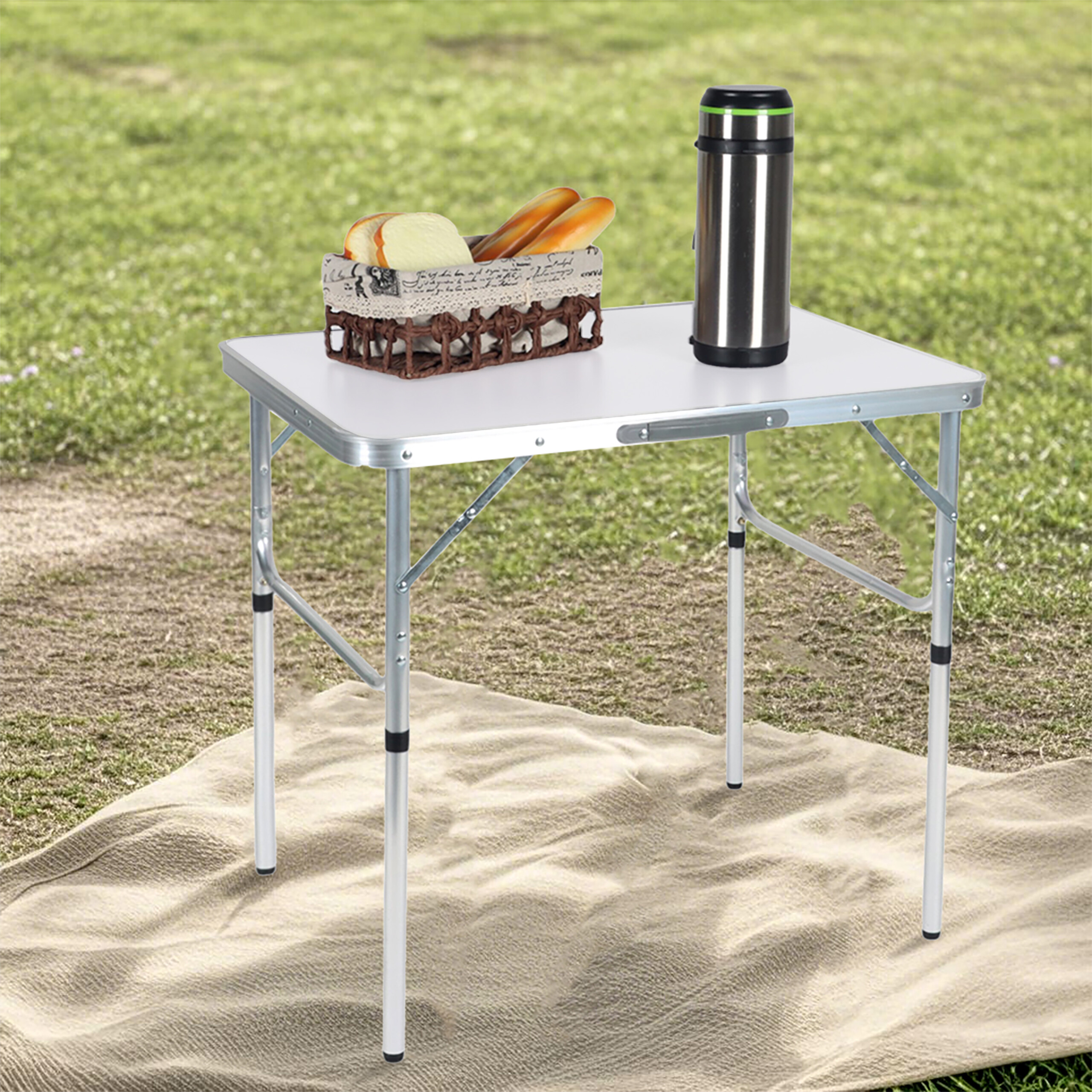 Ein weißer Klapptisch mit Brotkorb und Thermoskanne steht auf einer Decke im Gras.