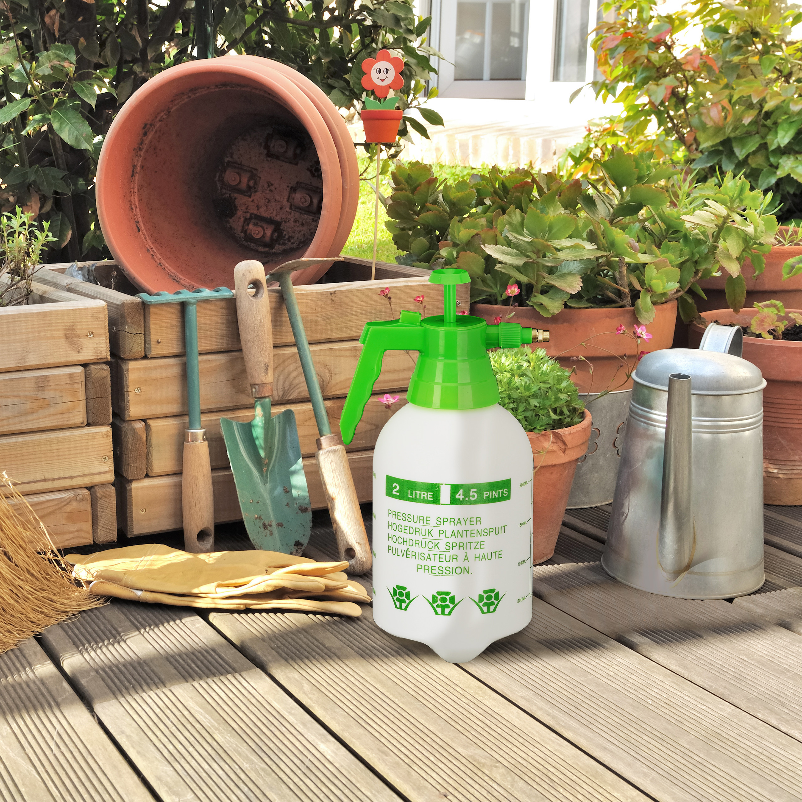 Gartenzubehör wie Drucksprüher, Schaufel, Gießkanne und Blumentöpfe auf Holzterrasse.