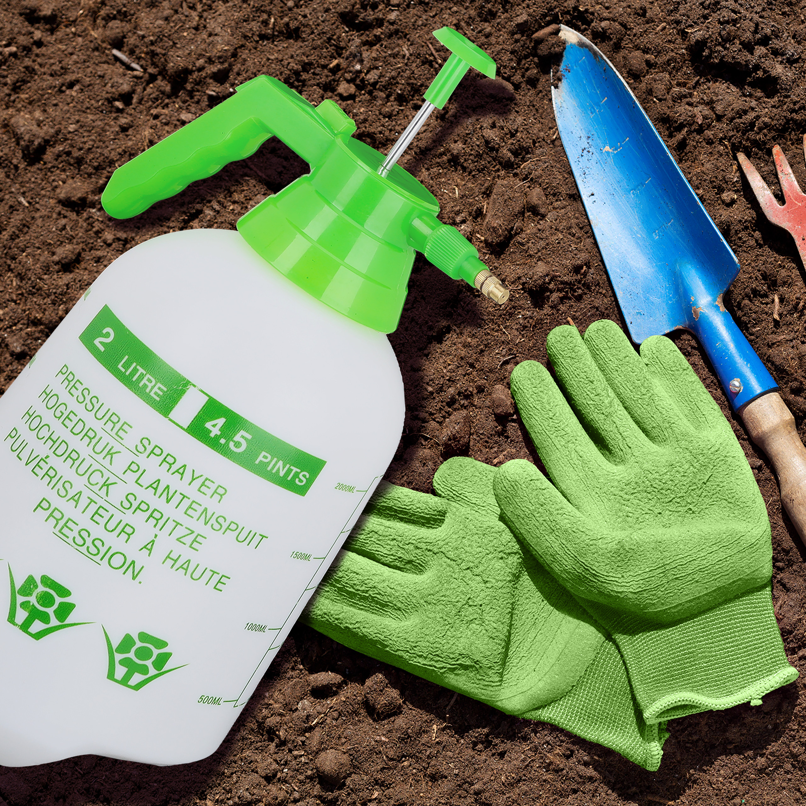 Gartenzubehör auf Erde: ein Drucksprüher, grüne Handschuhe und eine blaue Schaufel.