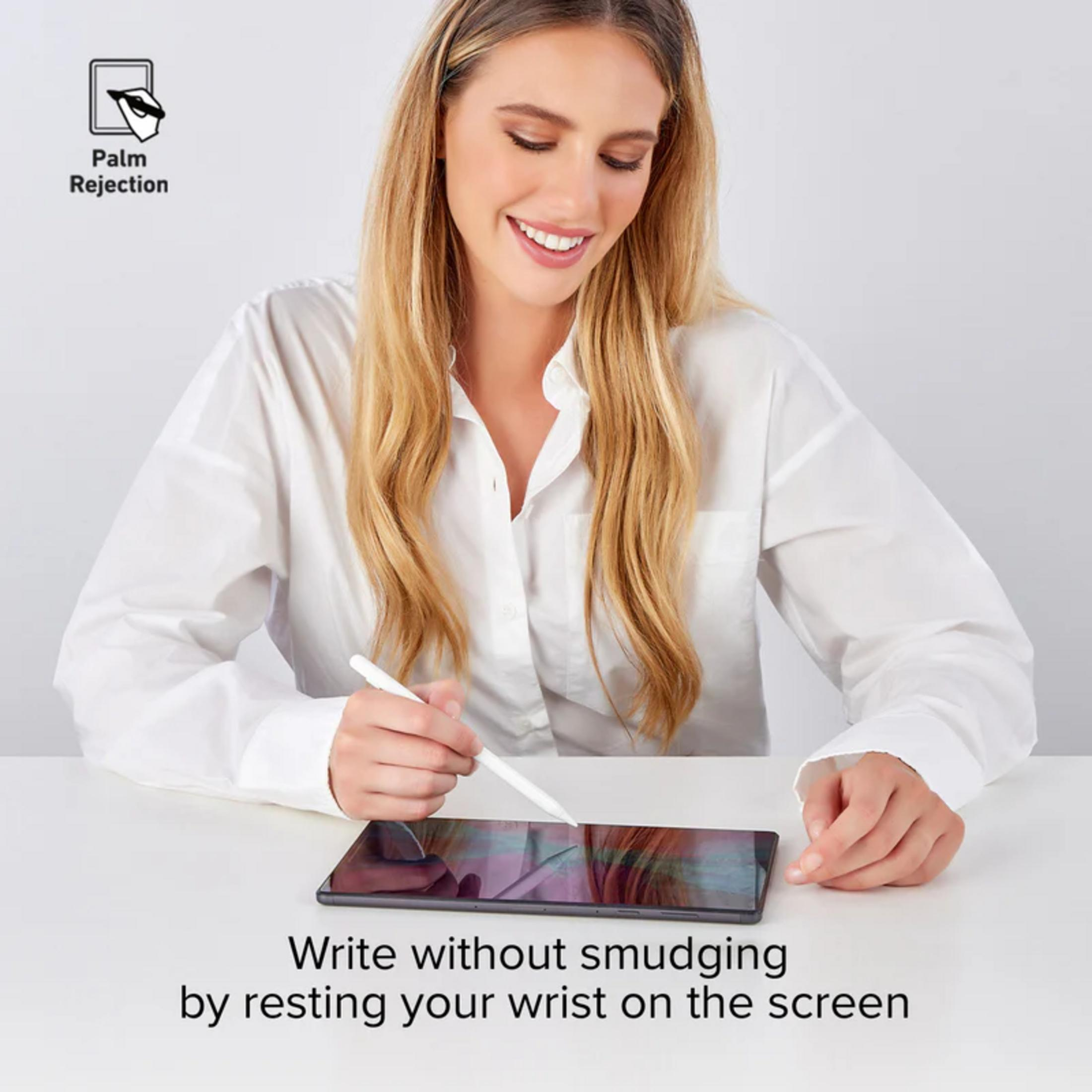 Una donna bionda con una camicia bianca siede a un tavolo e scrive con un pennino su un tablet.