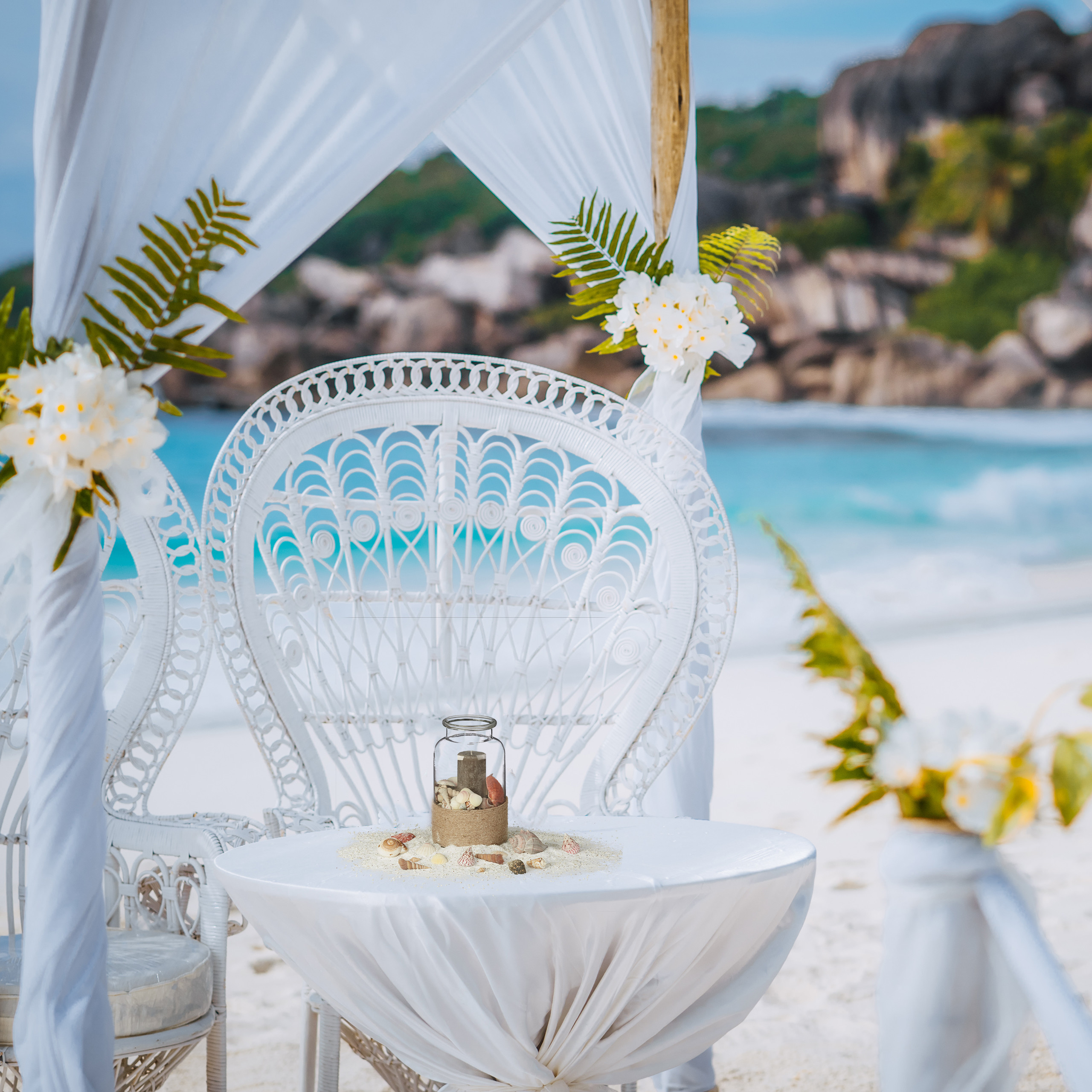 Weißer Hochzeitstisch und Stühle unter Baldachin am Strand mit Meerblick.