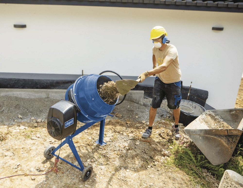 Arbeiter in Schutzkleidung nutzt eine blaue Betonmischmaschine auf einer Baustelle.