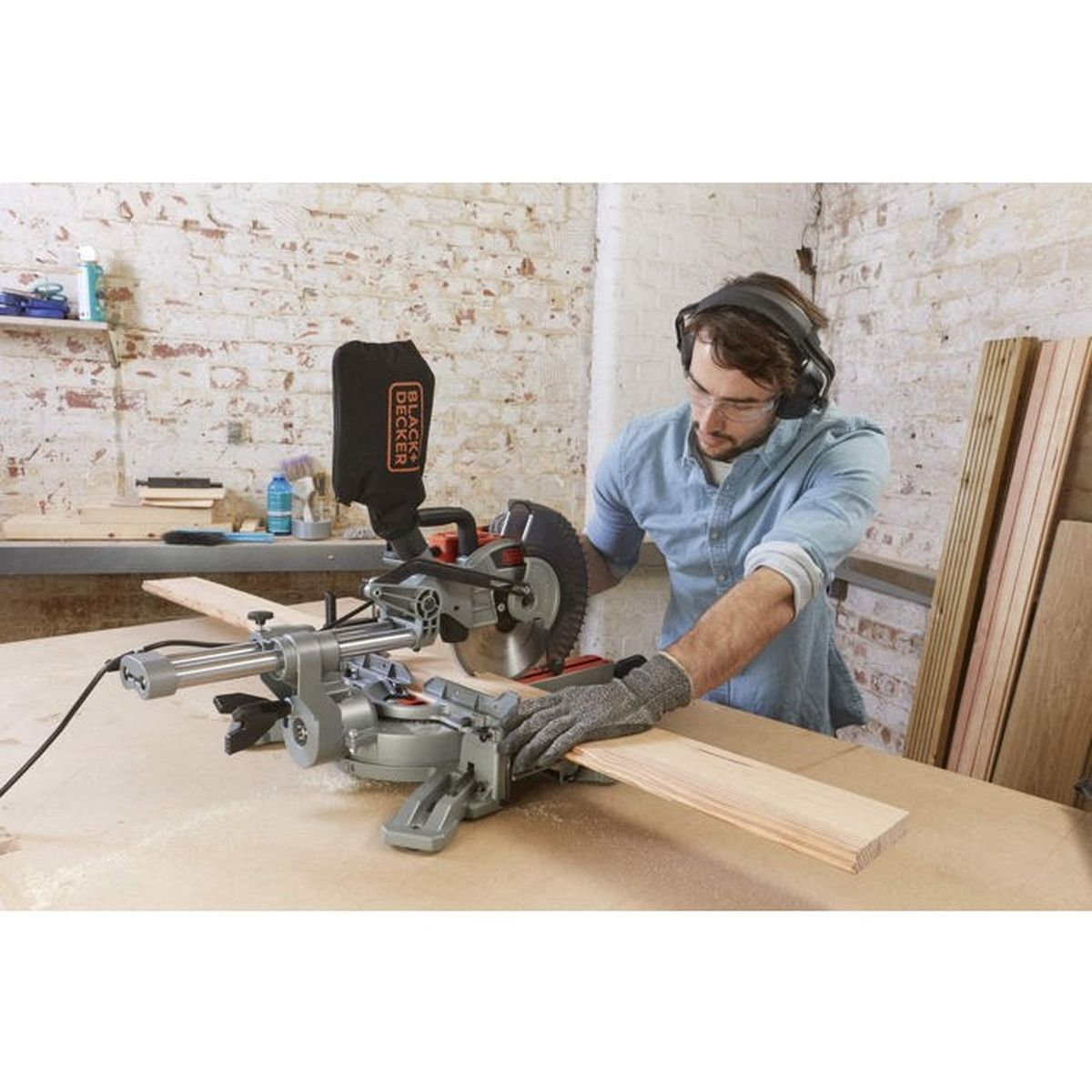 Ein Mann mit Schutzausrüstung schneidet in einer Werkstatt mit einer Kappsäge ein Holzbrett.