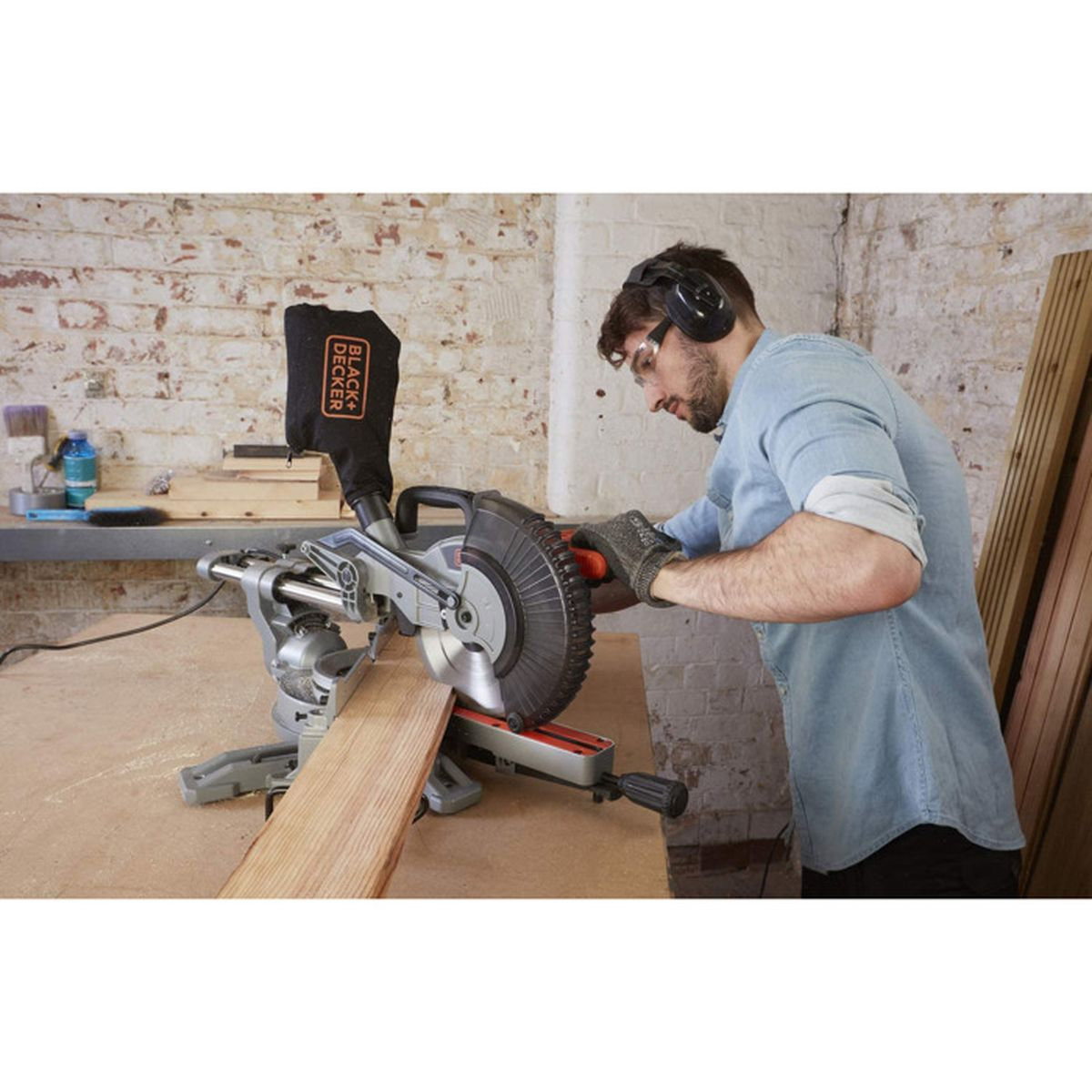 Ein Mann mit Schutzkleidung schneidet in einer Werkstatt mit einer Gehrungssäge ein Holzbrett.