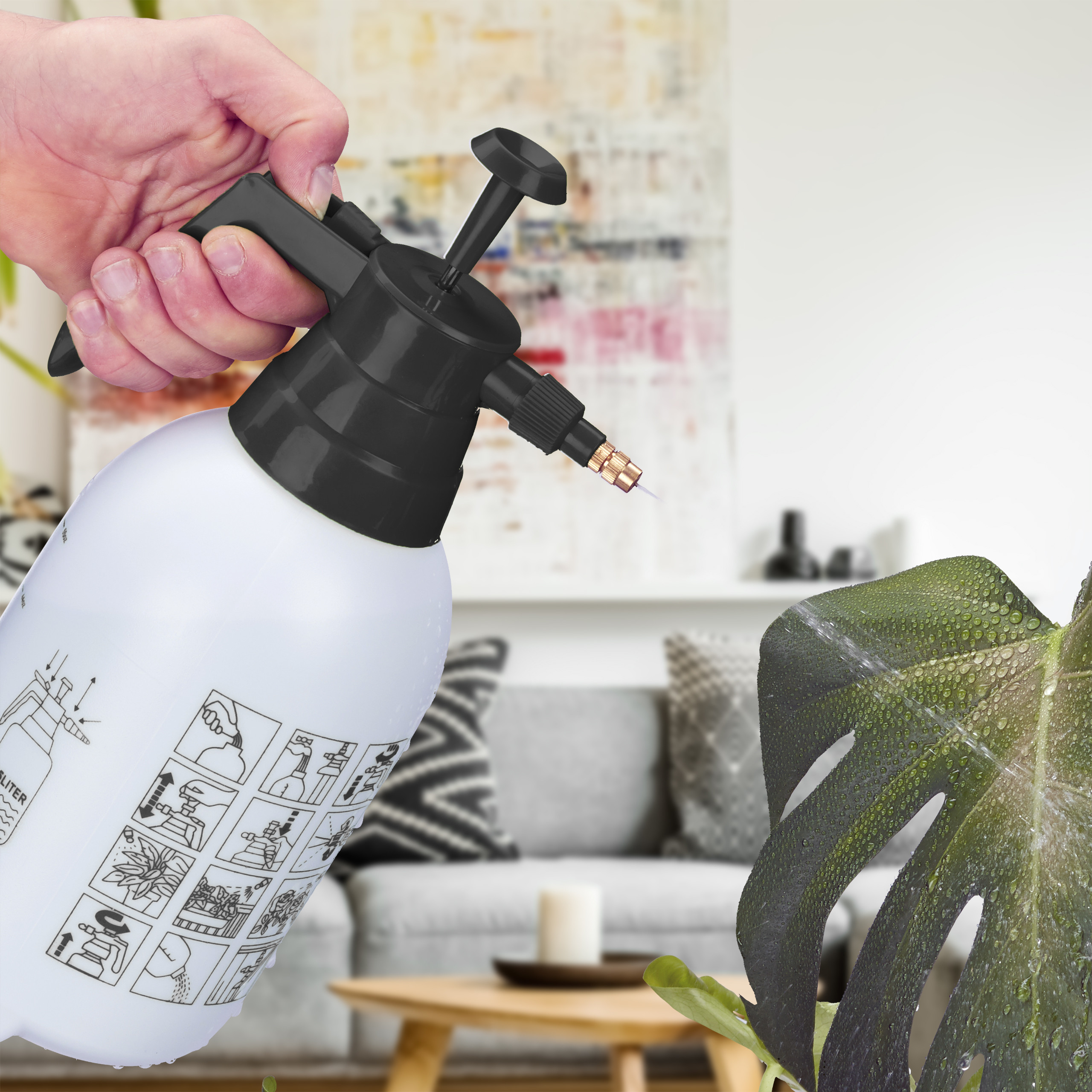 Eine Hand hält eine weiße Pumpsprühflasche und besprüht ein großes grünes Pflanzenblatt in einem hellen Wohnzimmer.