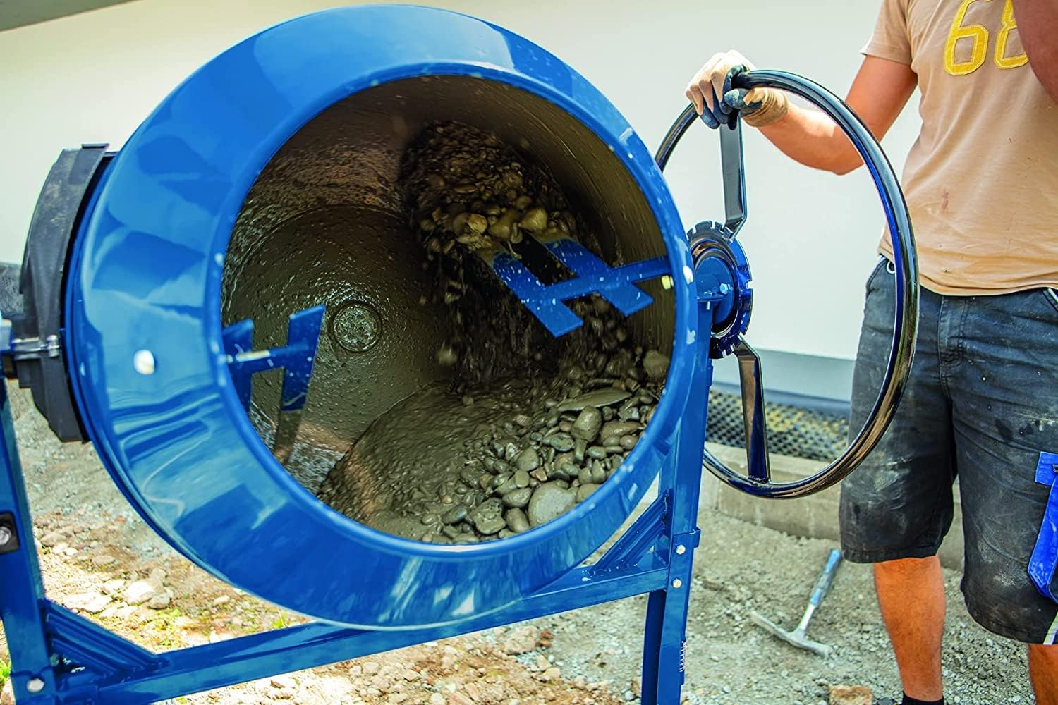 Ein Arbeiter bedient eine blaue Betonmischmaschine auf einer Baustelle.