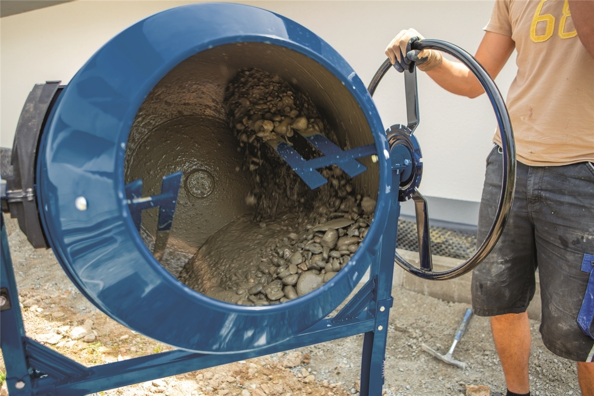 Ein Arbeiter bedient eine blaue Betonmischmaschine, in der sich Kies und Zement vermengen.