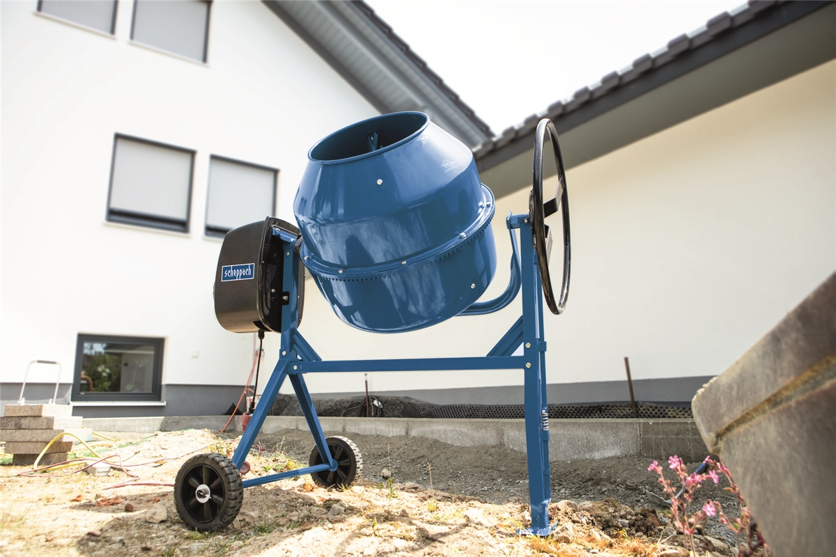 Ein blauer Betonmischer steht auf einer Baustelle vor einem modernen Haus.