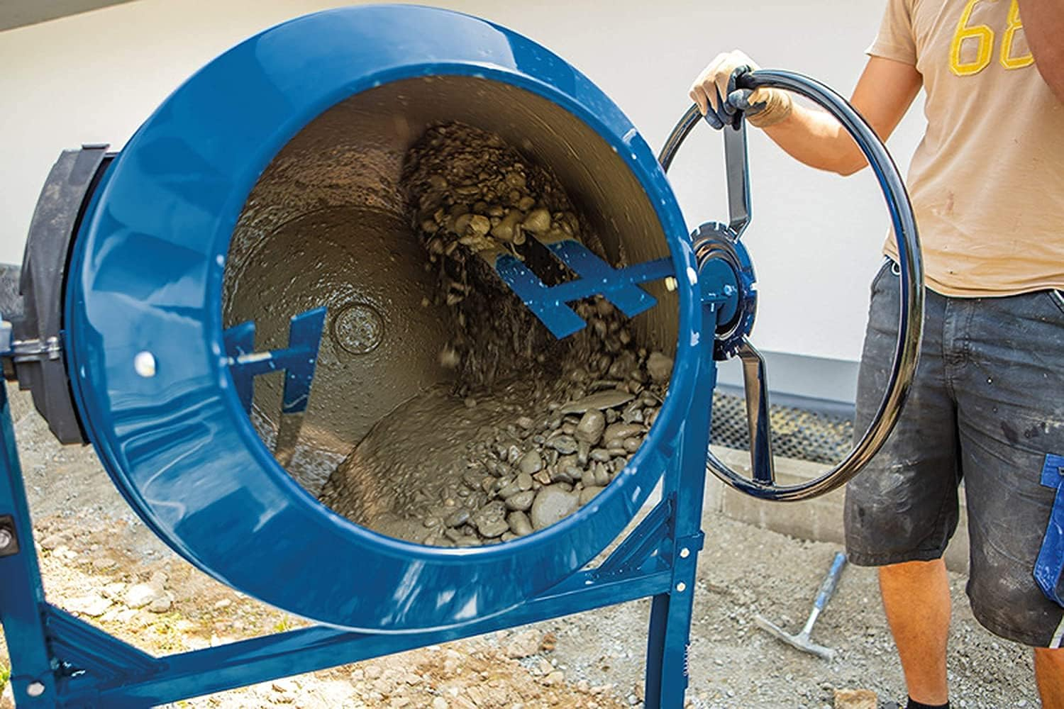 Ein Arbeiter bedient einen blauen Zementmischer mit nassem Beton und Steinen.