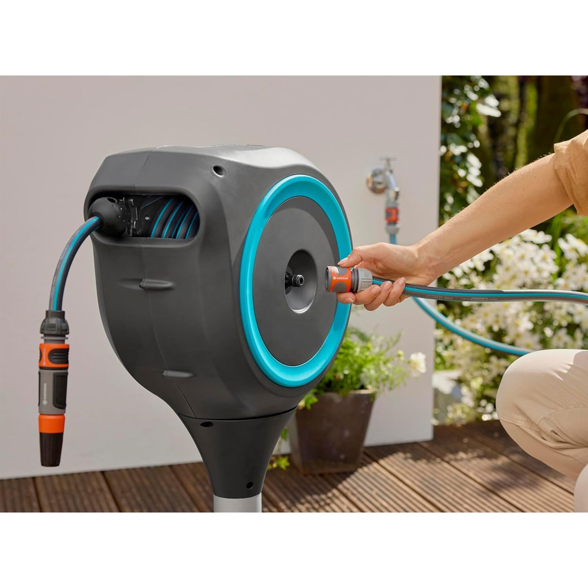 Eine Person zieht einen blauen Gartenschlauch aus einer grauen Schlauchbox mit türkisfarbenem Ring.
