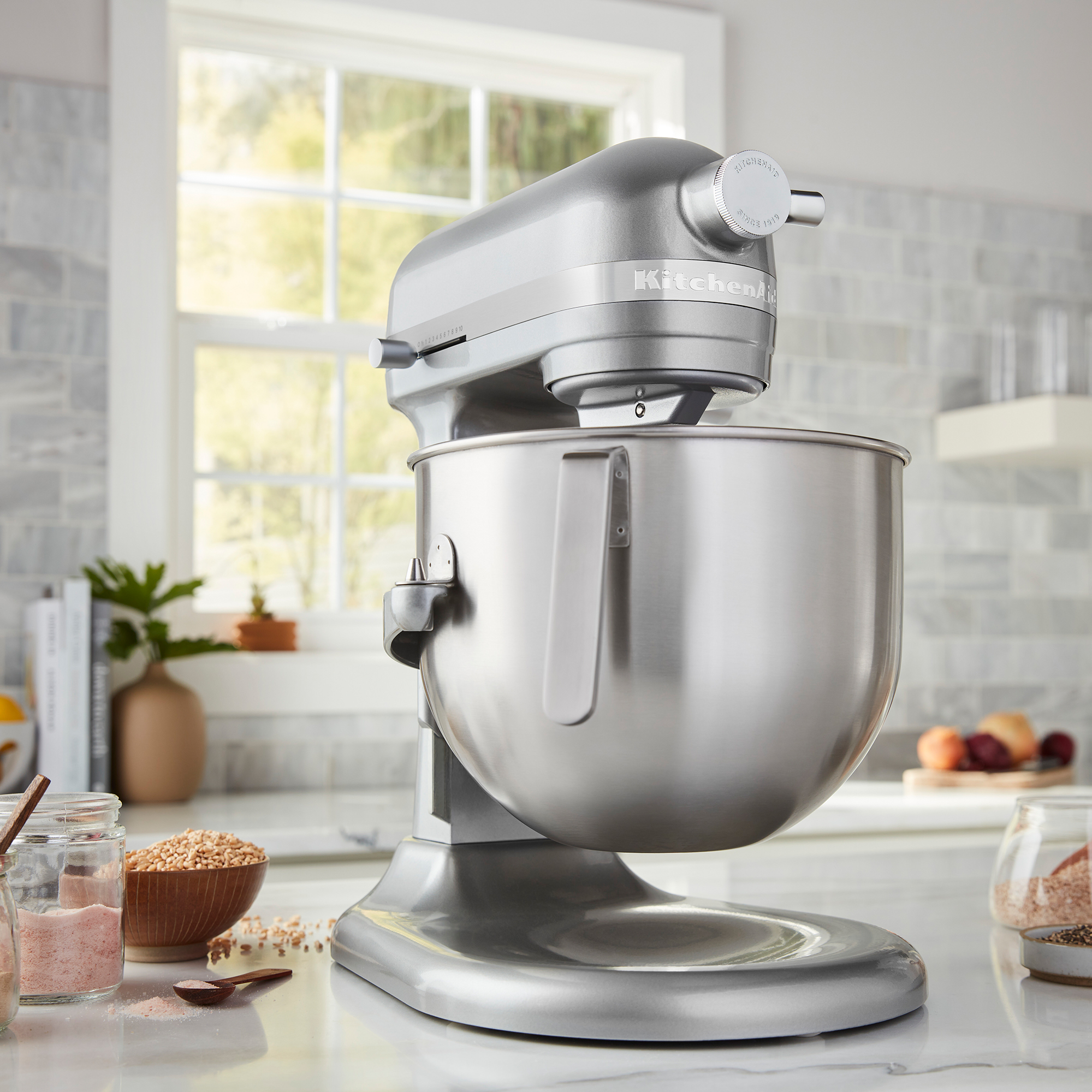 Eine silberne KitchenAid-Küchenmaschine steht auf einer Marmorarbeitsplatte in einer hellen Küche.