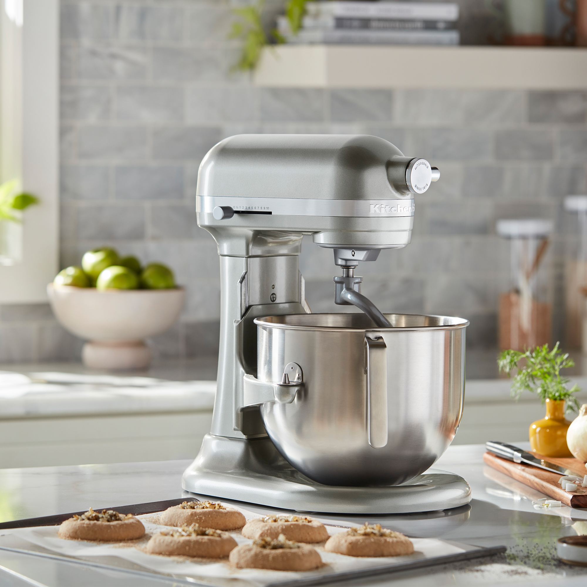 Ein silberner KitchenAid Standmixer steht auf einer Küchentheke neben Gebäck und einem Schneidebrett.