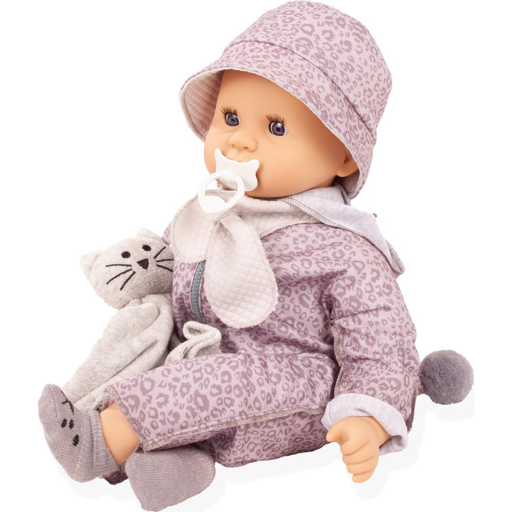 Una bambola con vestiti e cappello leopardati rosa e ciuccio siede tenendo un peluche grigio.