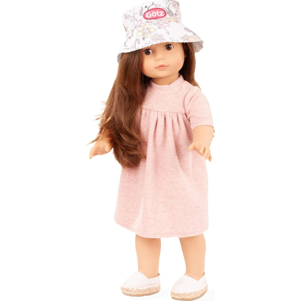 Una bambola con capelli castani indossa un abito rosa, un cappello fantasia e scarpe bianche su sfondo bianco.