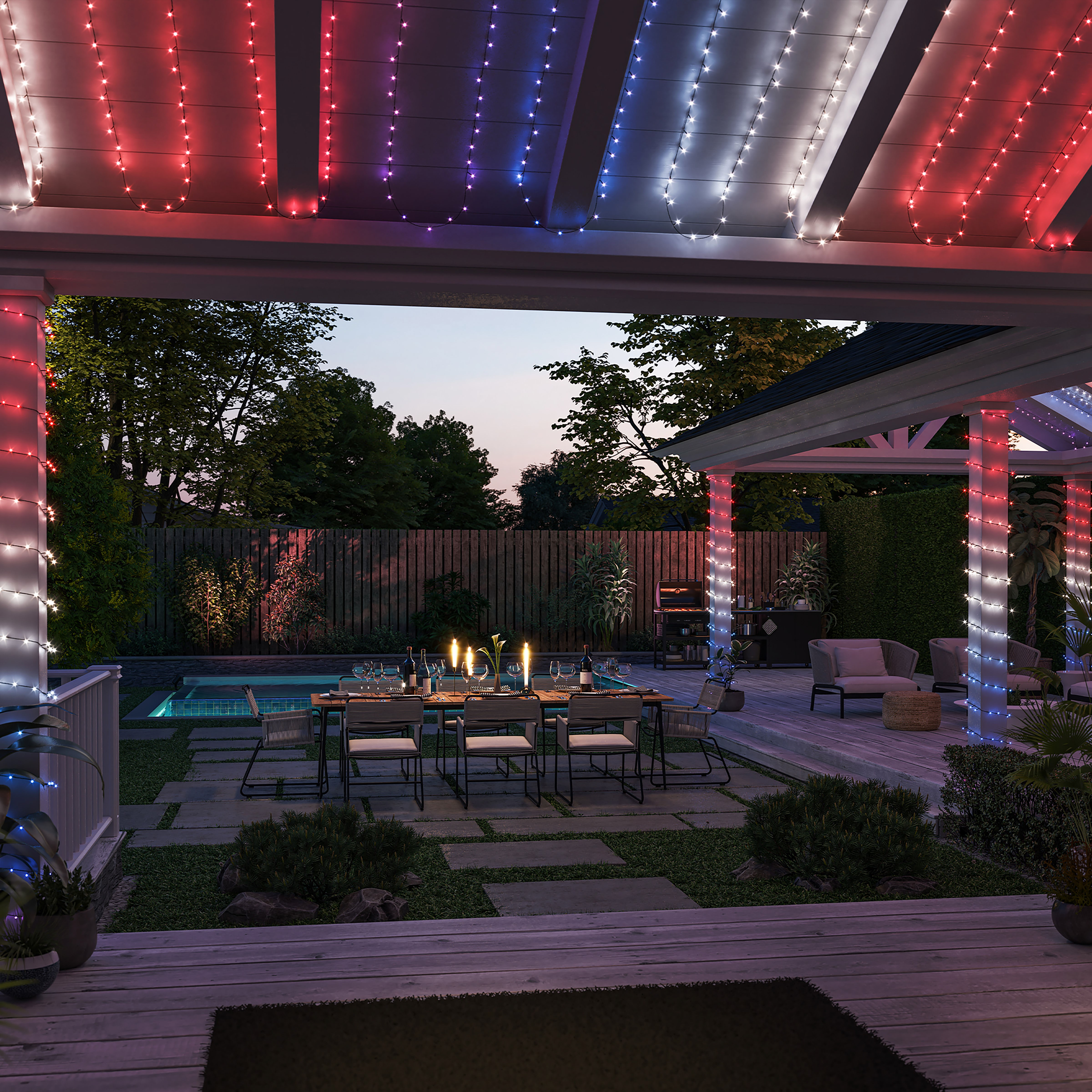 Terrasse in der Dämmerung mit rot-weiß-blauen Lichterketten, Esstisch mit Kerzen, Pool und Grün.