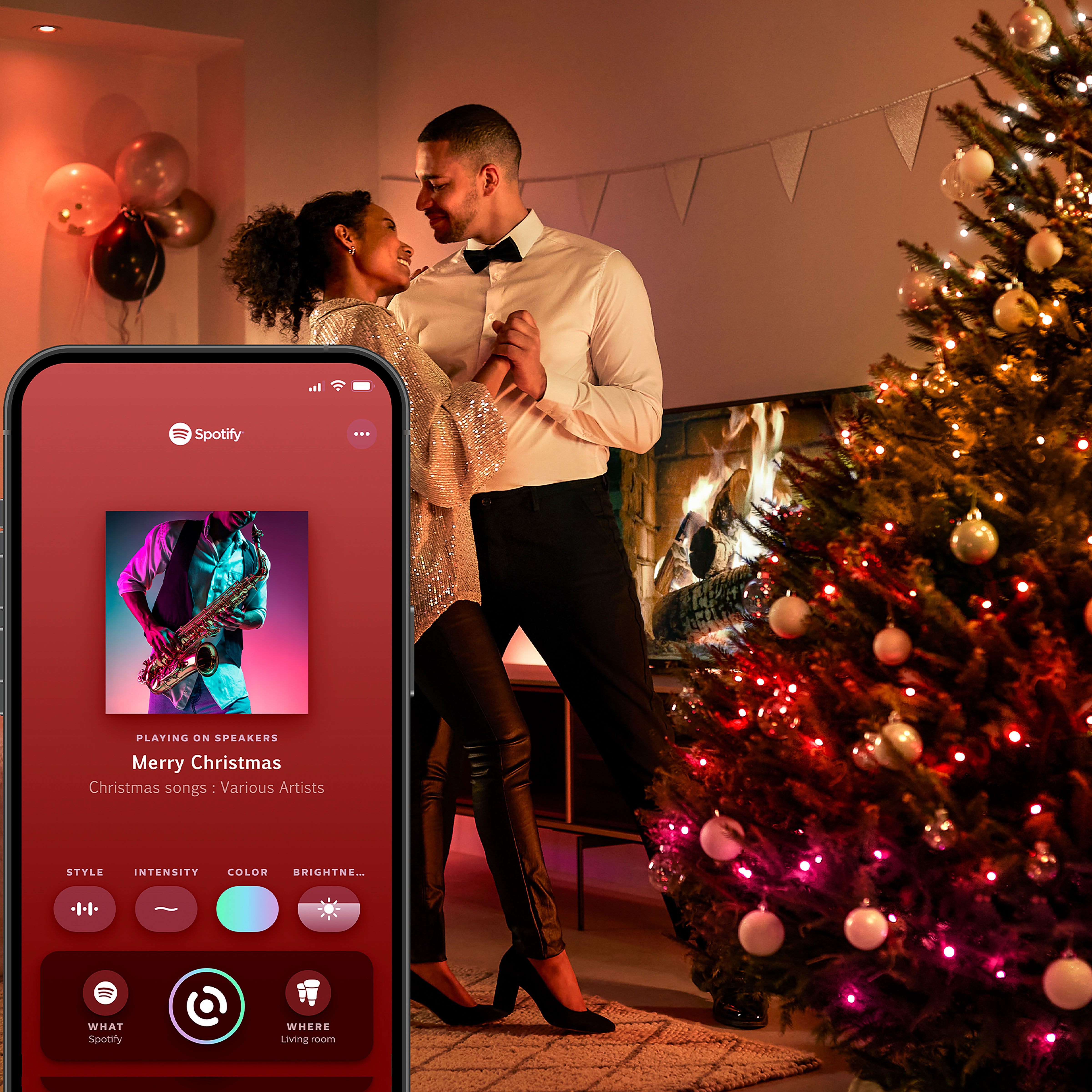 Ein Paar tanzt vor einem Weihnachtsbaum, während ein Smartphone Spotify steuert.