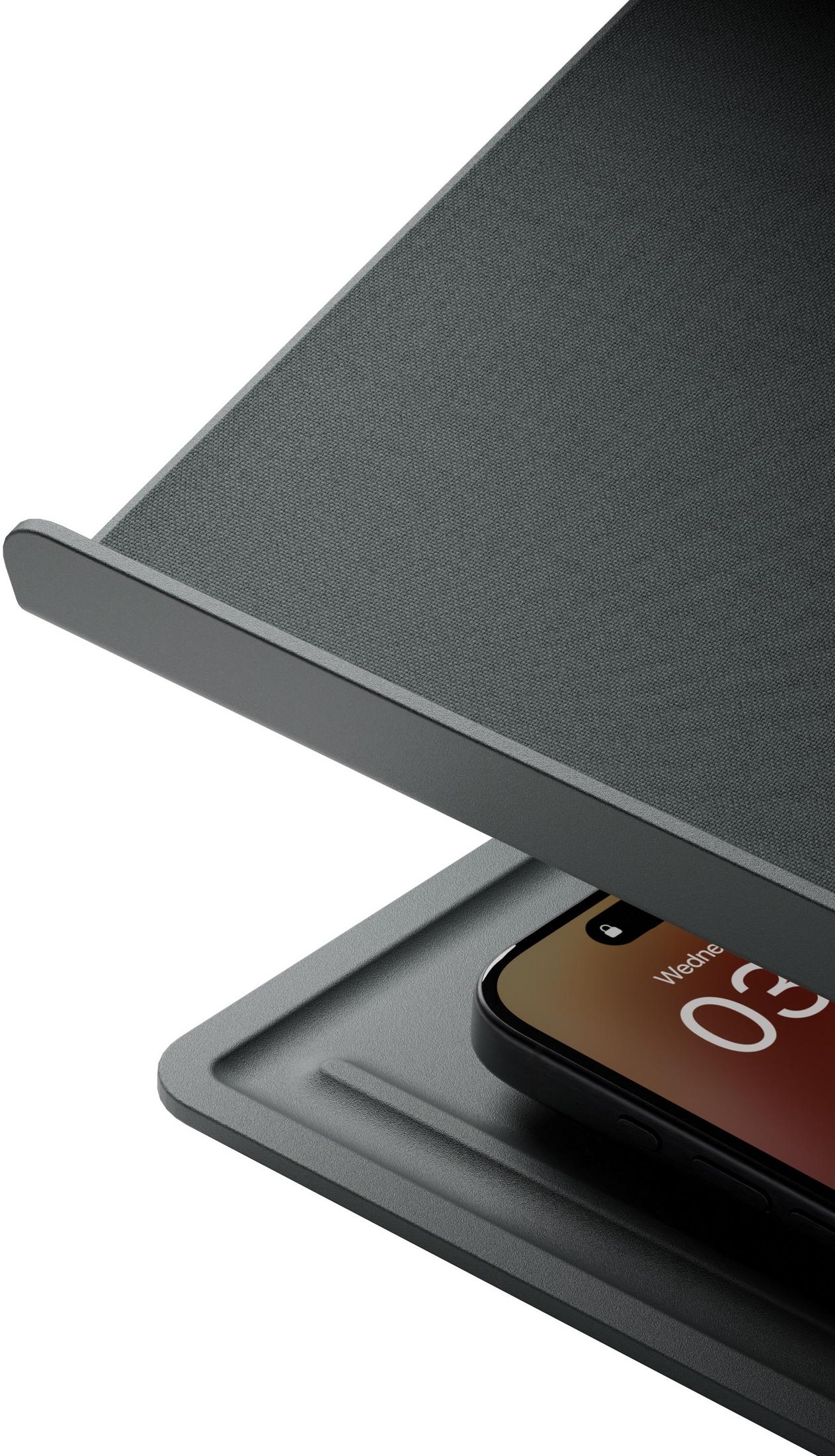 Smartfon spoczywa pod nachyloną, ciemną podstawką o fakturze.