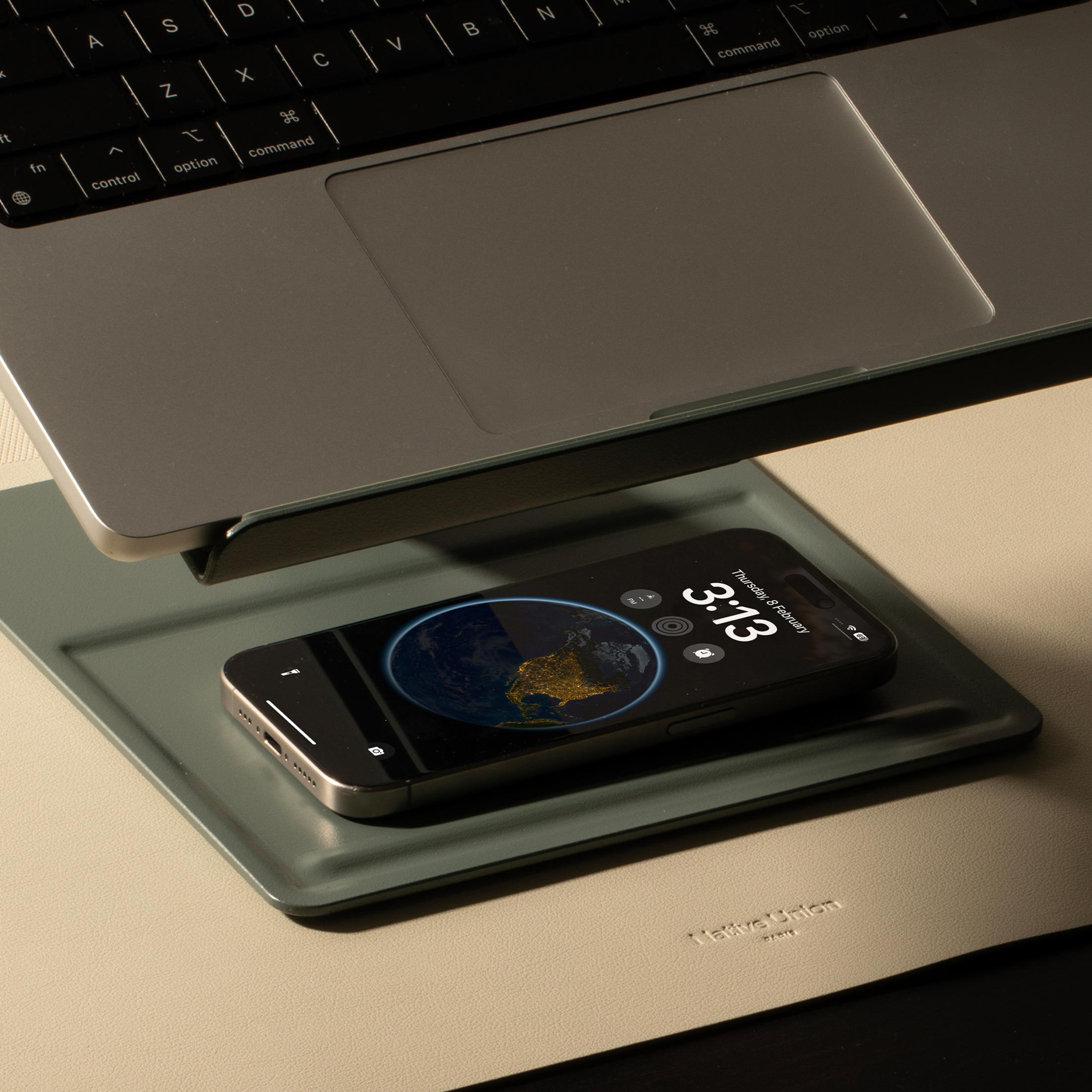 Smartfon z ekranem przedstawiającym Ziemię leży na zielonej podkładce pod laptopem.