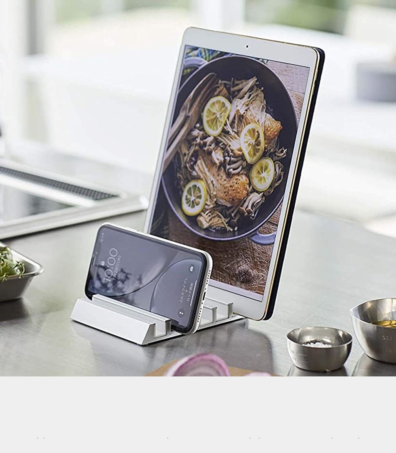 Srebrny metalowy stojak podtrzymuje tablet z przepisem i smartfon na blacie kuchennym.