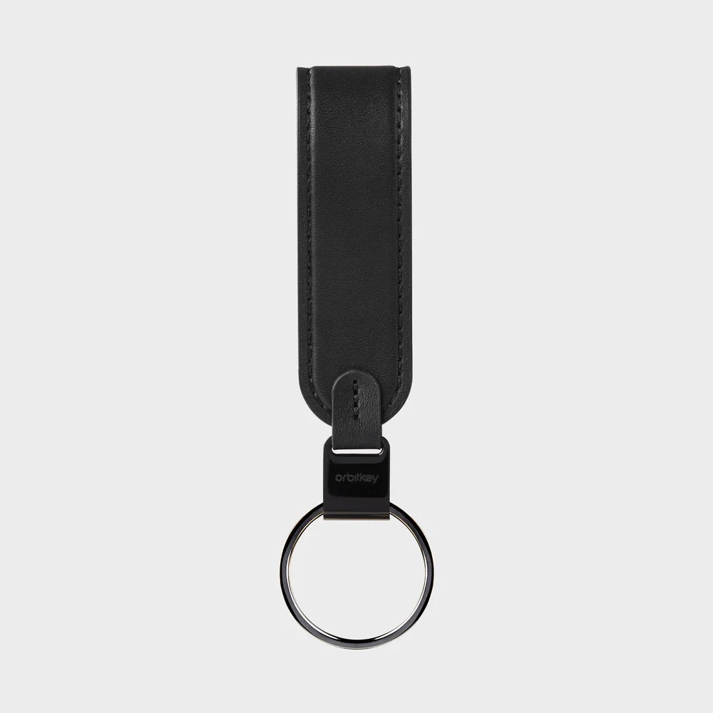 Czarny skórzany brelok z metalowym kółkiem i napisem Orbitkey na gładkim szarym tle.