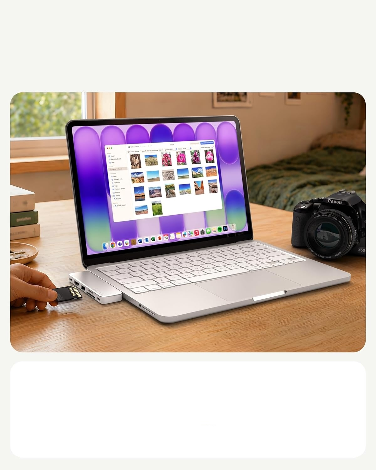 Ręka wsadza kartę SD do huba w srebrnym laptopie na biurku, obok aparat.