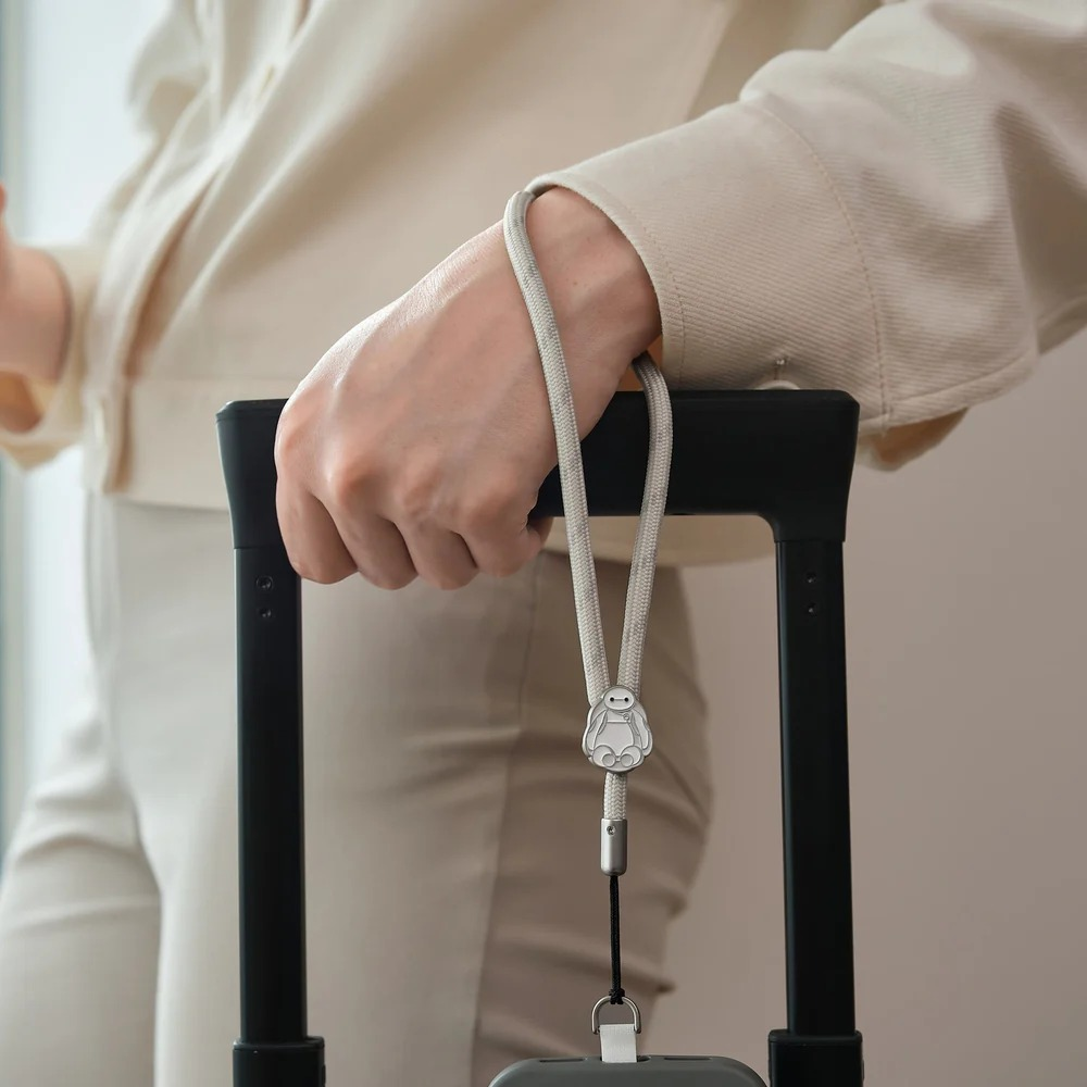Osoba w jasnych ubraniach trzyma rączkę walizki ze smyczą na nadgarstku.