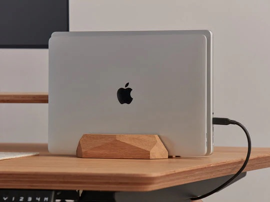 Zamknięty laptop na drewnianym stojaku na biurku z podłączonym kablem.