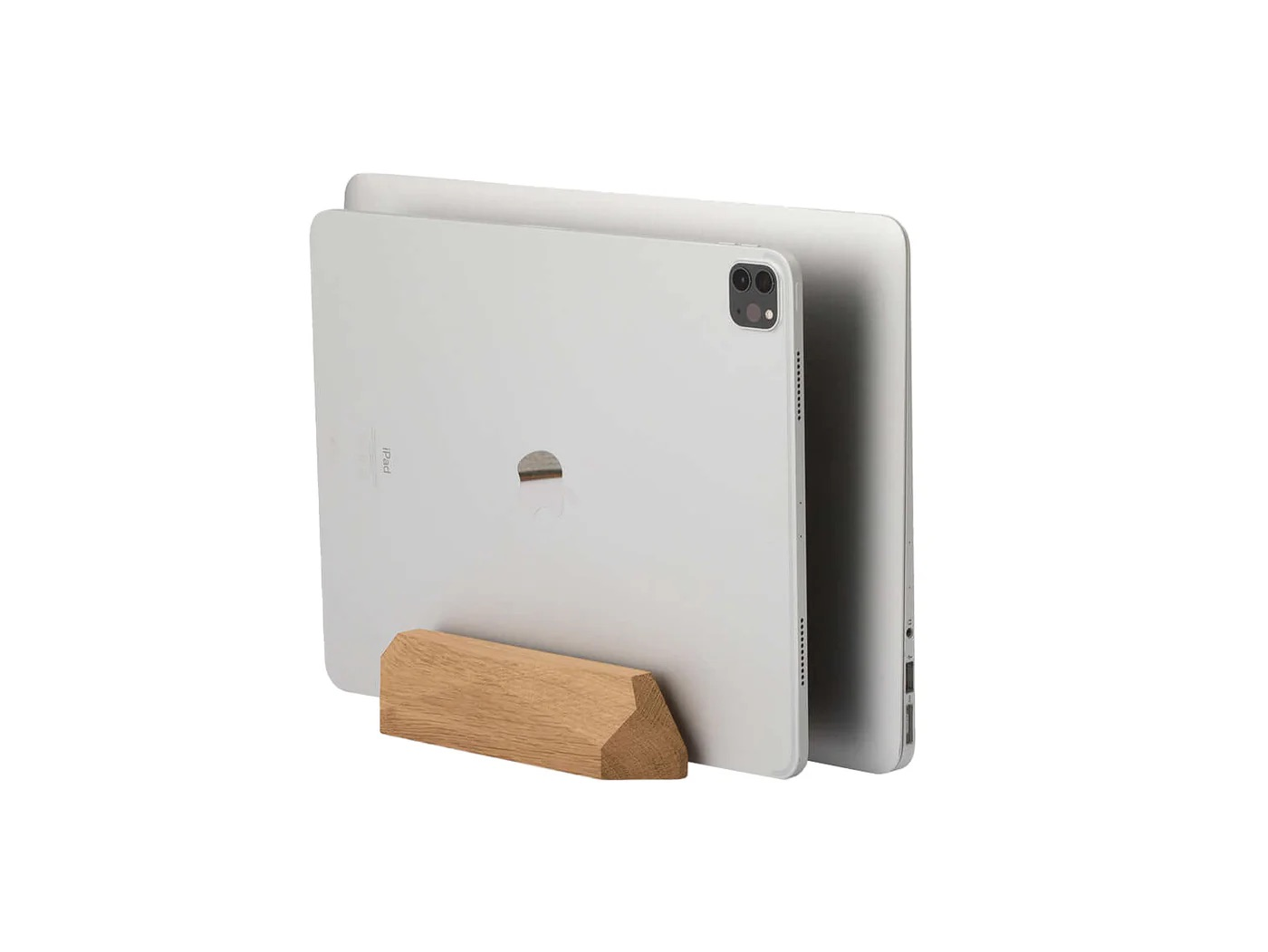 Srebrny laptop i tablet stoją pionowo w małym drewnianym stojaku na białym tle.