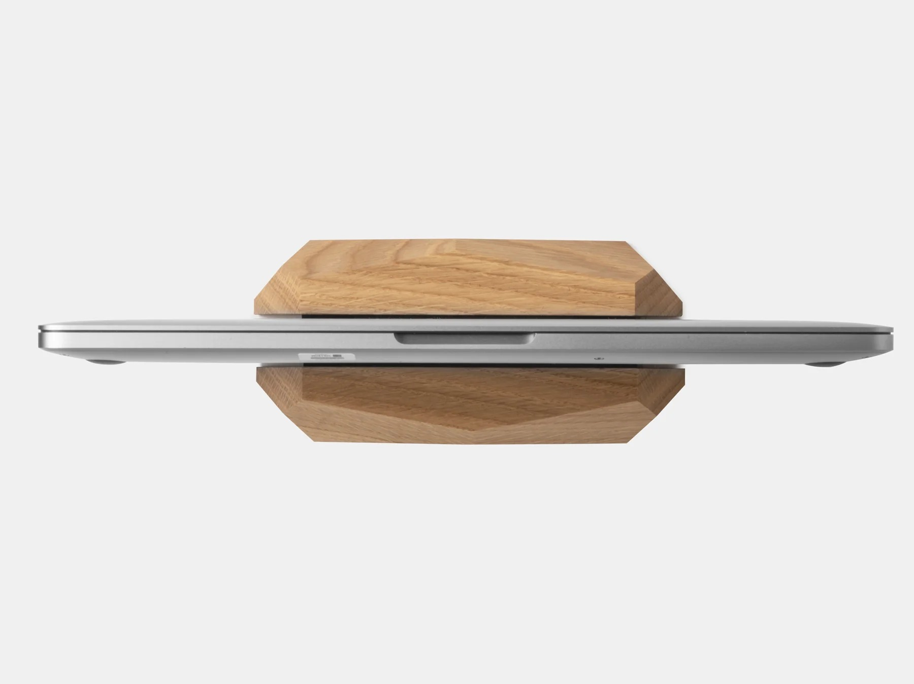 Zamknięty srebrny laptop stoi pionowo w drewnianym stojaku na białym tle.