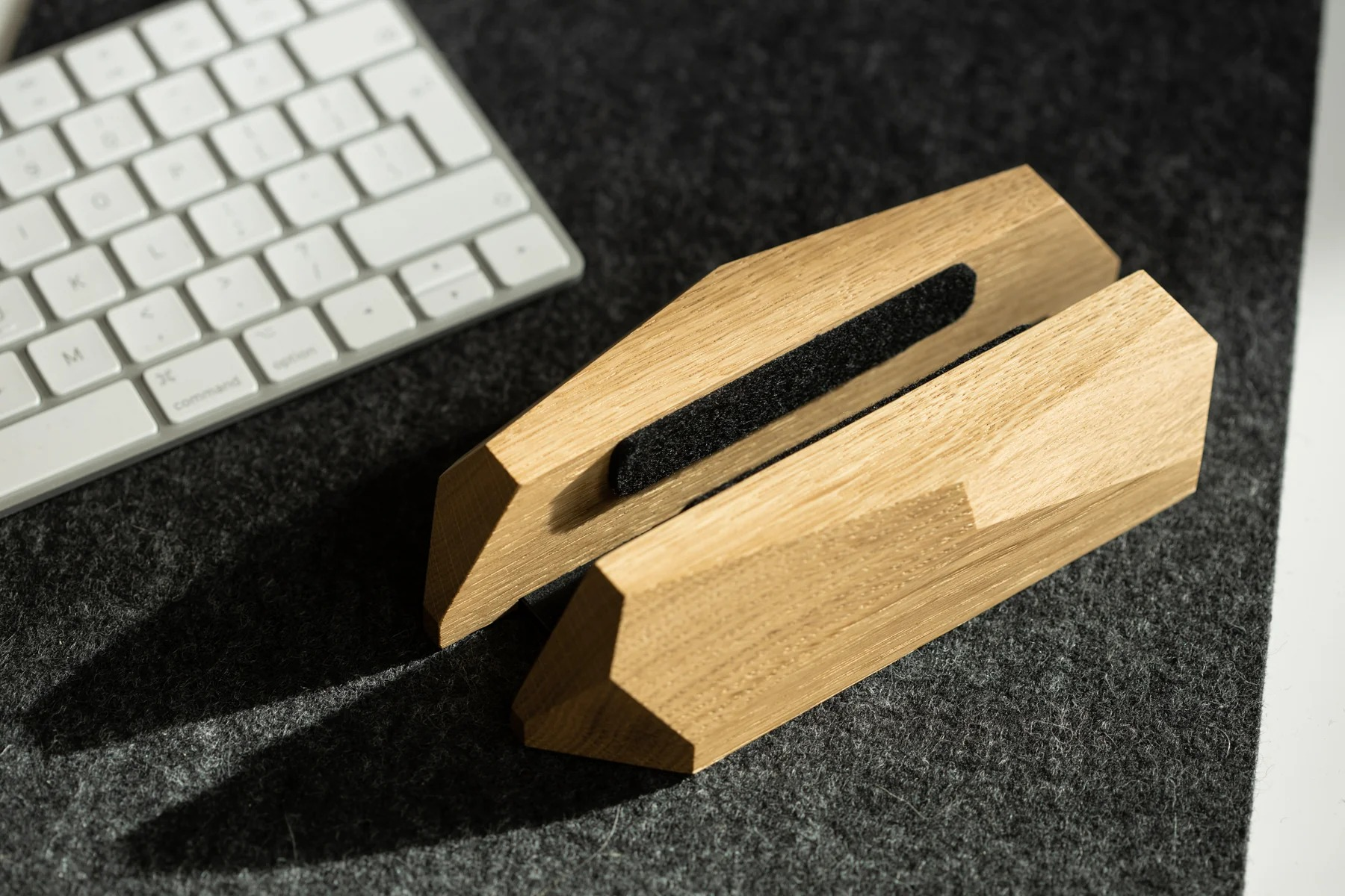 Drewniany stojak na laptopa z czarnym filcem stoi na ciemnej podkładce filcowej obok białej klawiatury.