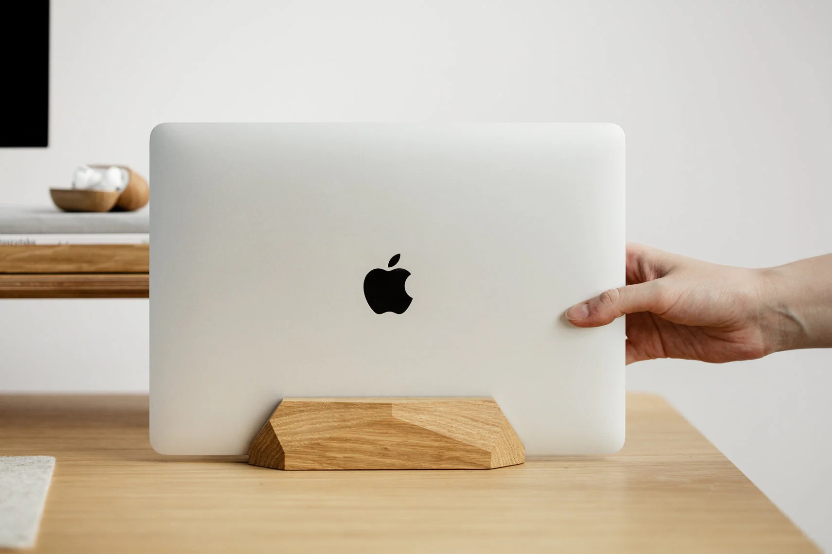 Ręka umieszcza zamknięty laptop w drewnianym stojaku na biurku.