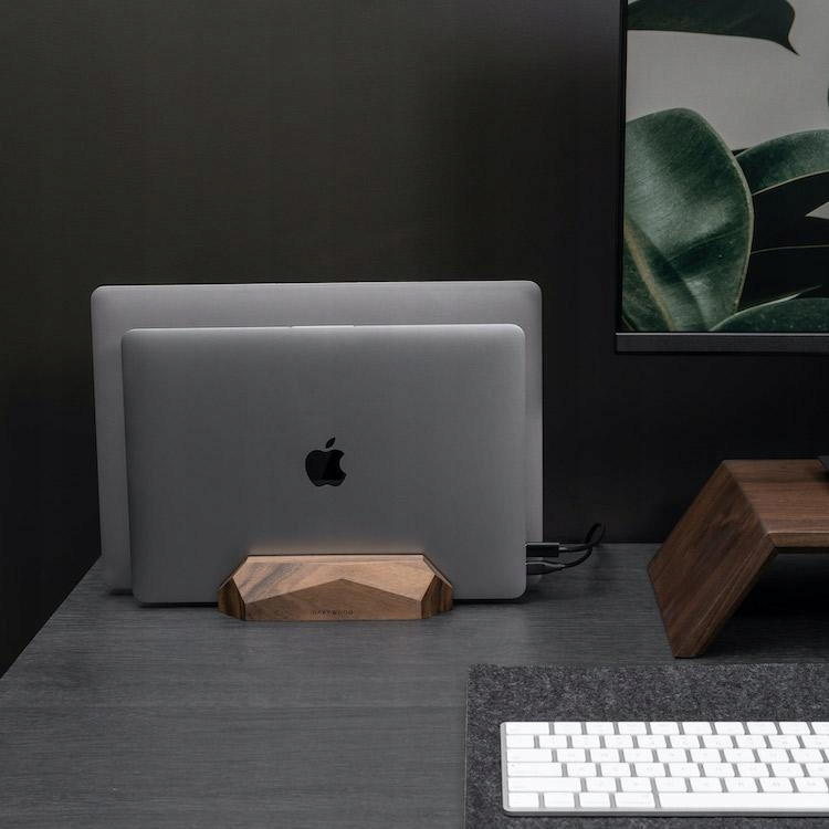 Dwa laptopy stoją na drewnianym stojaku na ciemnym biurku.