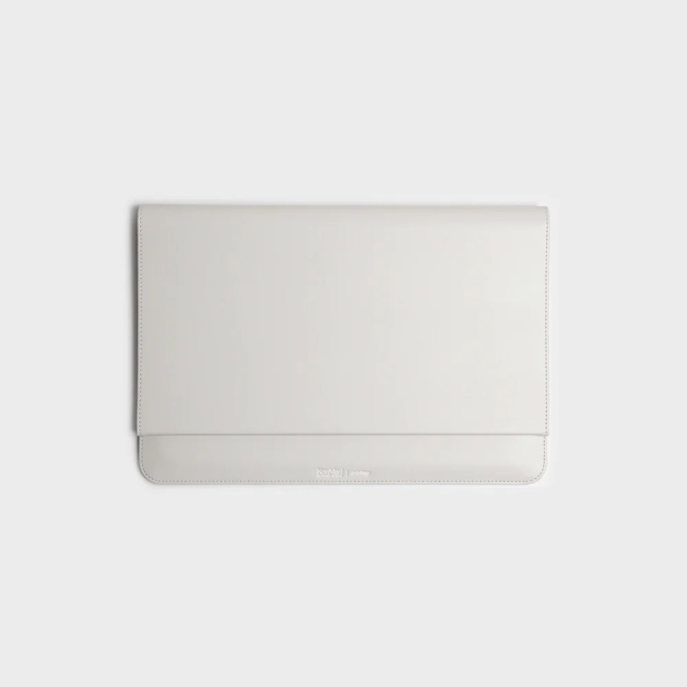 Zamknięte, jasnoszare skórzane etui na laptopa z subtelnymi przeszyciami i wytłoczonym logo na gładkim tle.
