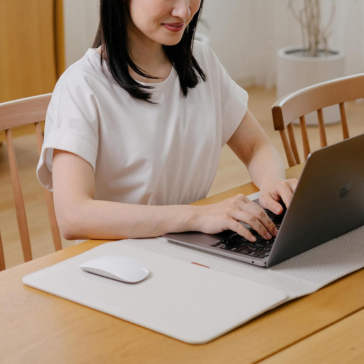 Kobieta w białej koszuli pisze na laptopie przy drewnianym stole.