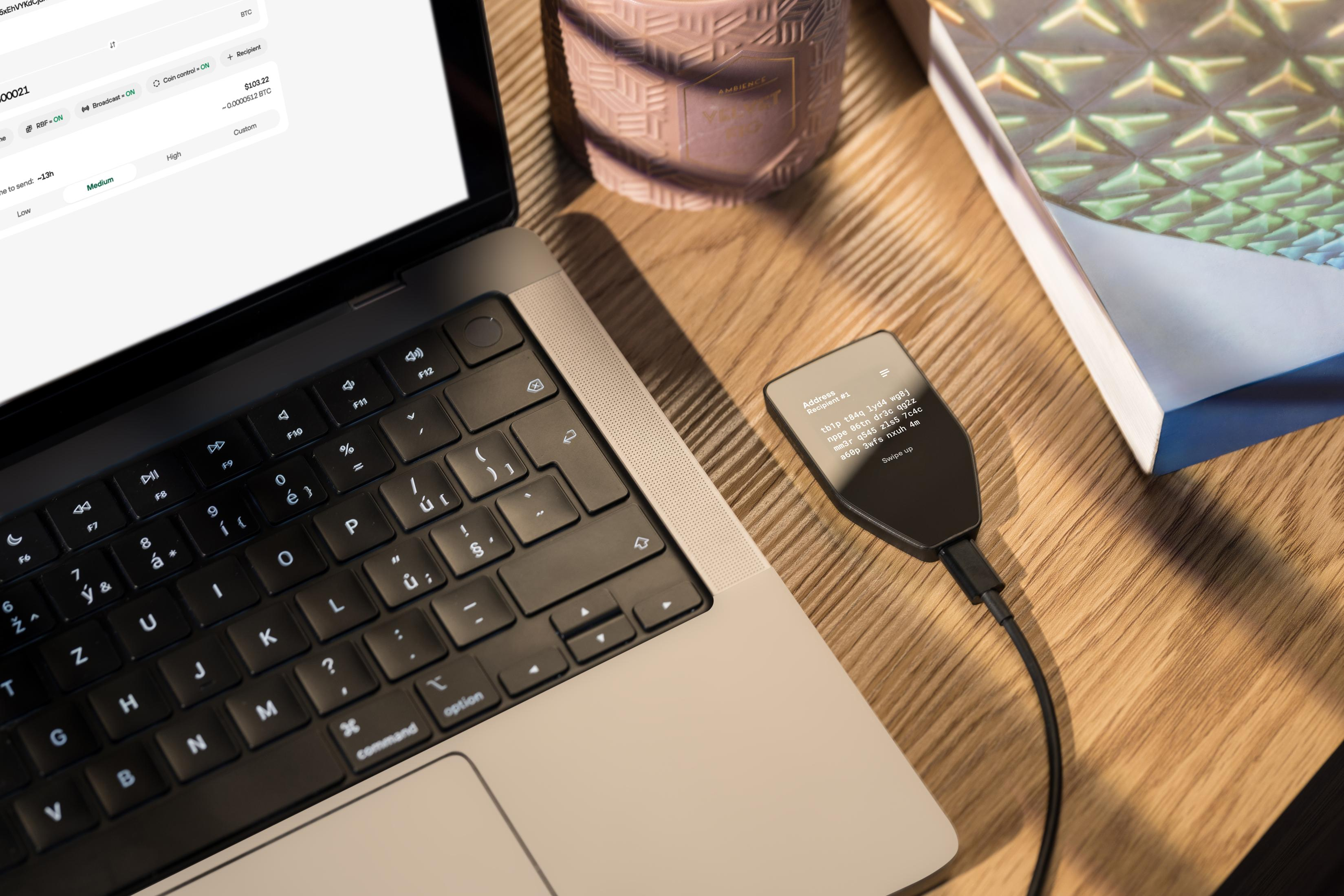 Kryptograficzny portfel sprzętowy podłączony kablem do laptopa na drewnianym biurku.