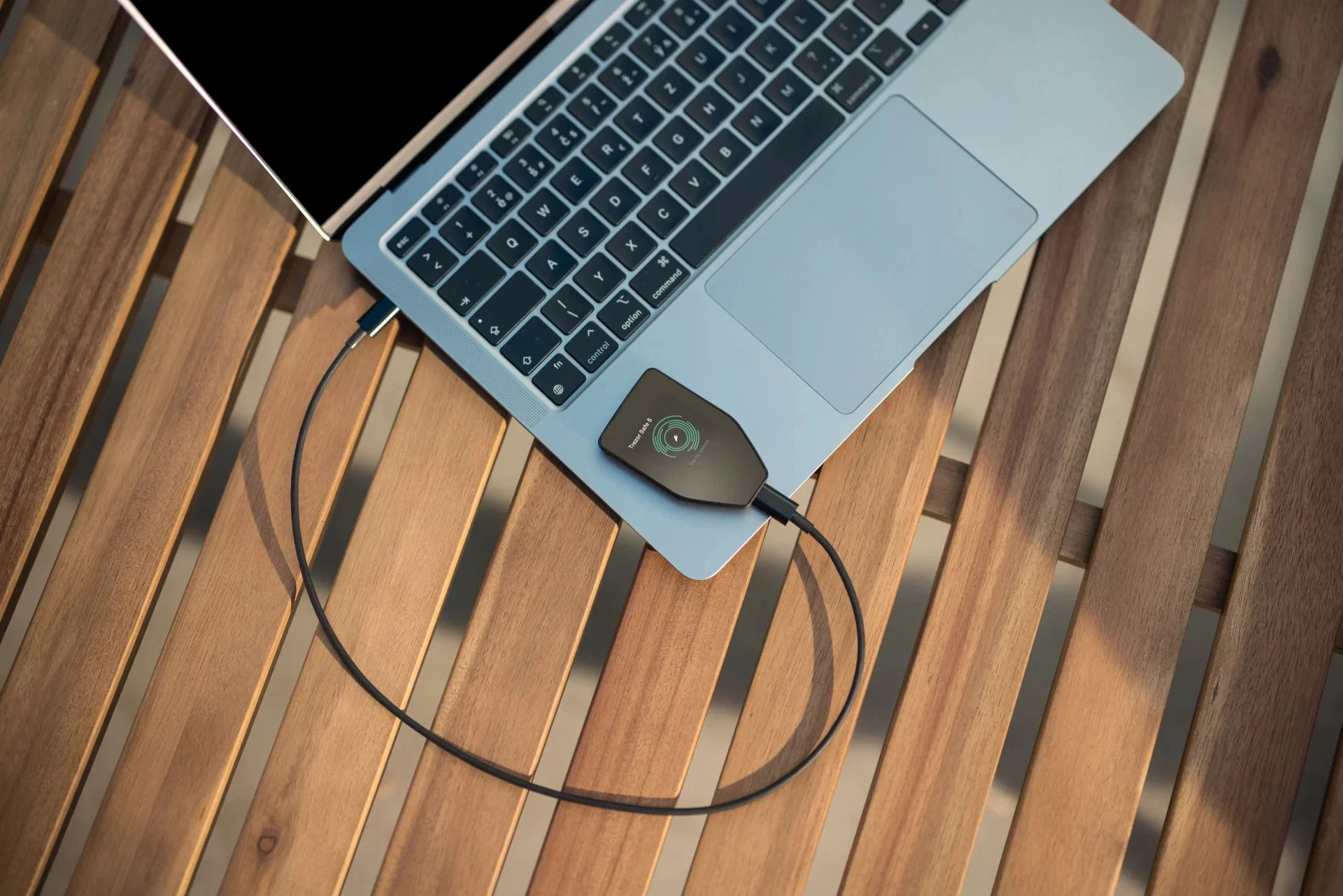 Un laptop argento e un portafoglio hardware crypto nero con cavo su un tavolo di legno.