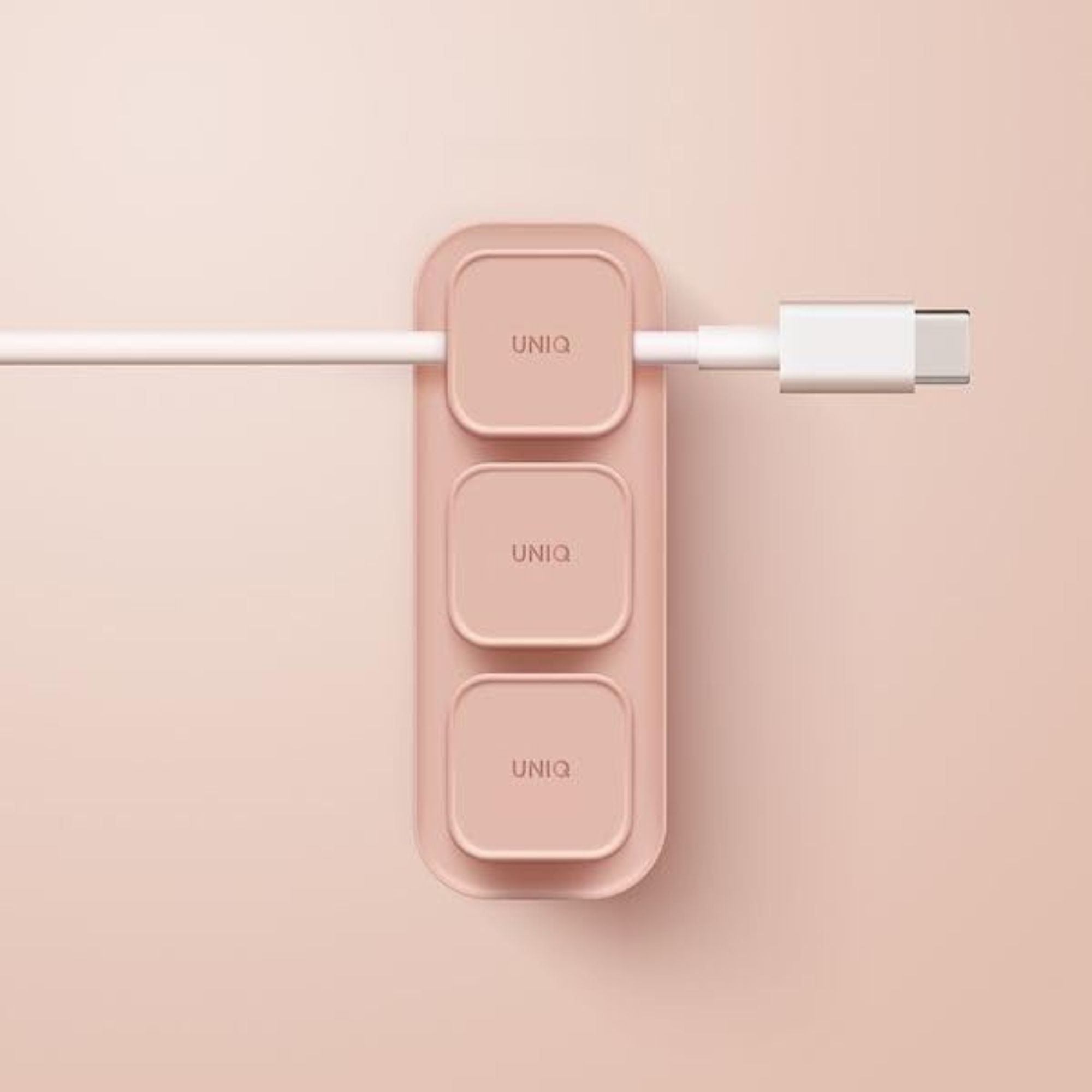 Różowy organizer do kabli z trzema kwadratowymi slotami przytrzymuje biały kabel USB.