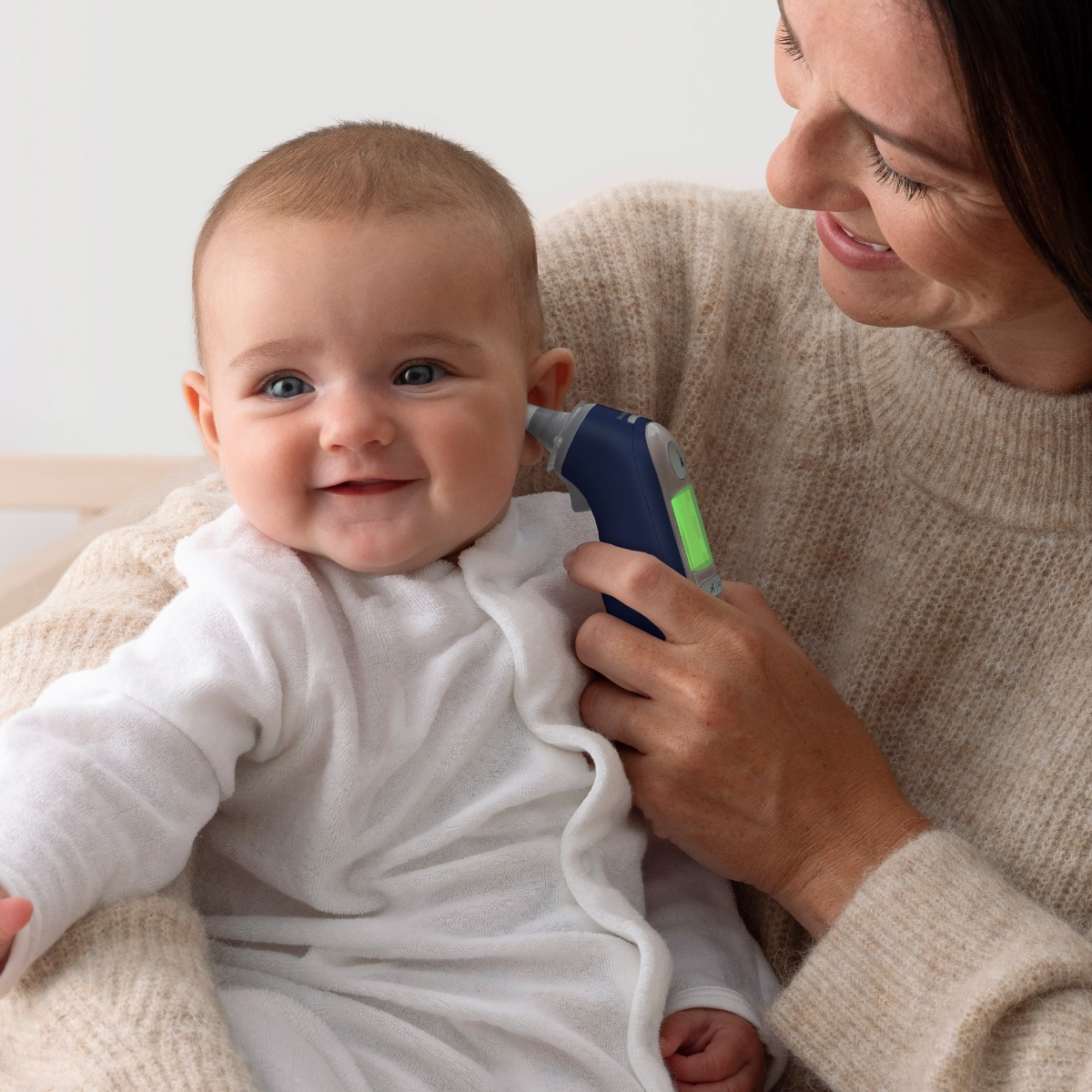 Eine Frau misst mit einem digitalen Ohrthermometer die Temperatur eines lächelnden Babys.