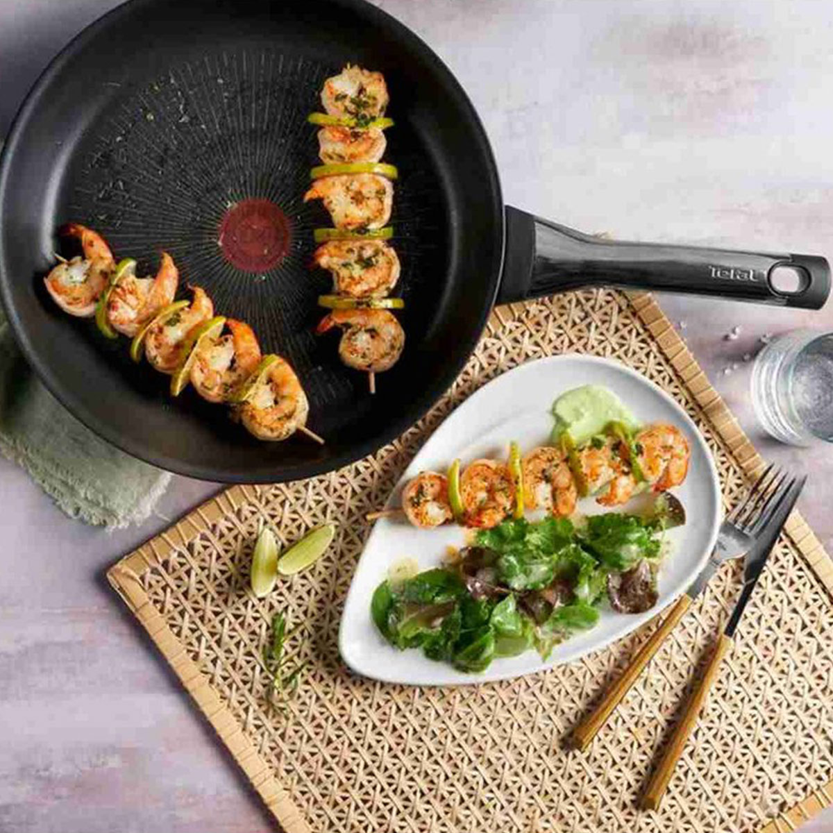 Brochetas de camarones a la parrilla con rodajas de lima en una sartén y en un plato con ensalada.