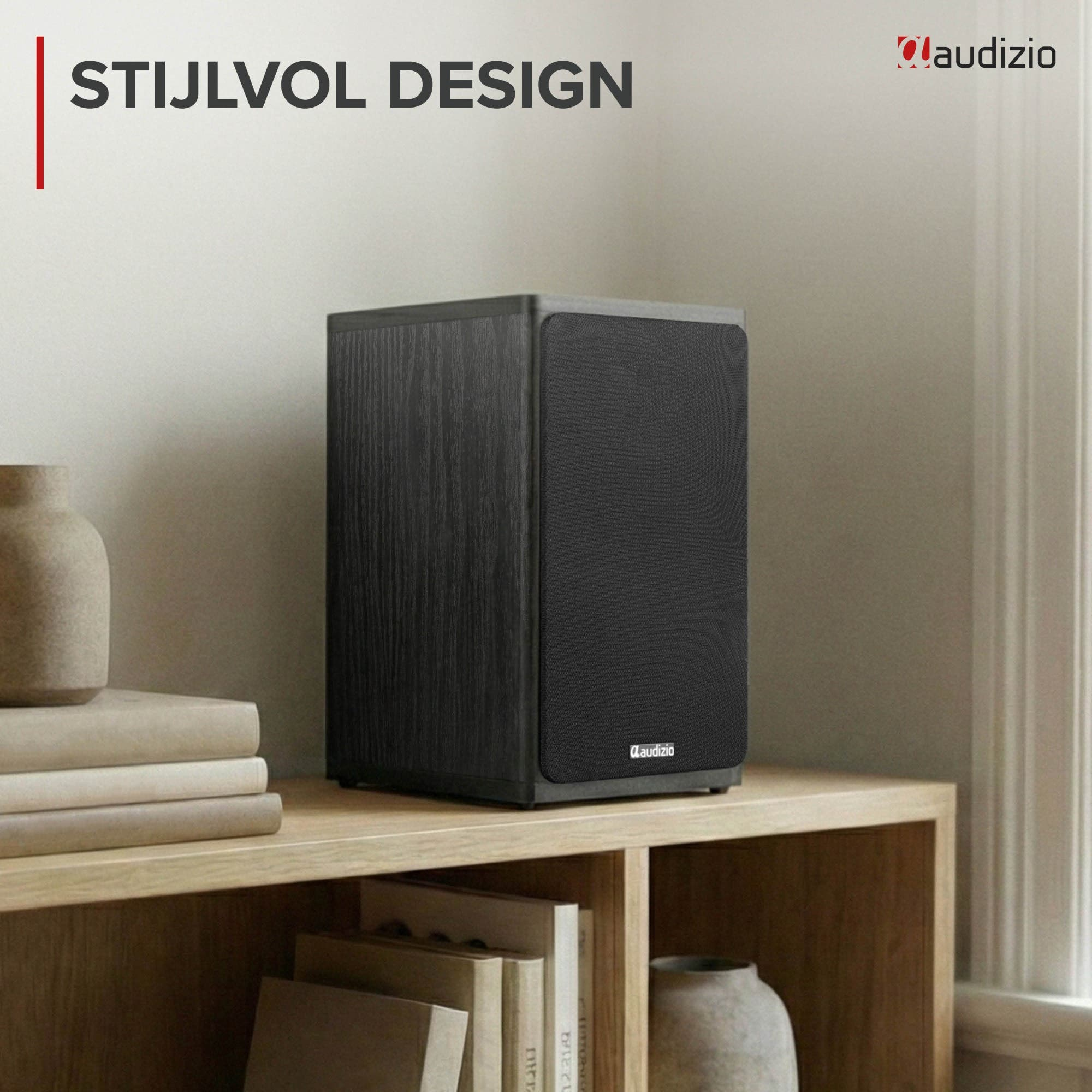 Un altavoz Audizio negro en una estantería de madera junto a libros apilados y un jarrón de cerámica.